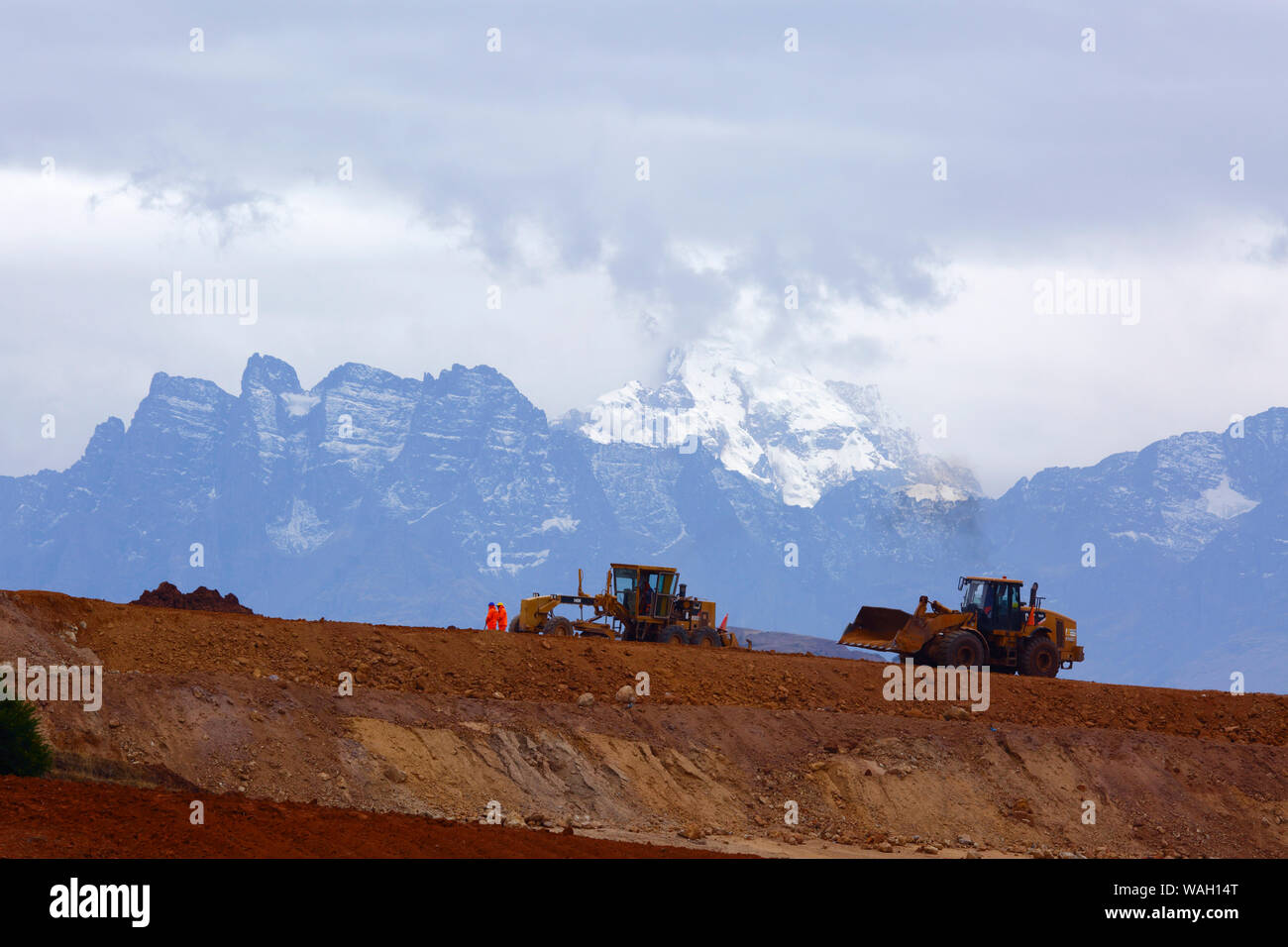 Heavy machinery working moving earth, the start of construction at the site of a new international airport at Chinchero for Cusco and Machu Picchu. In the background is Mt Sawasiray, one of the peaks of the Cordillera Urubamba mountain range. Cusco Region, Peru Stock Photo