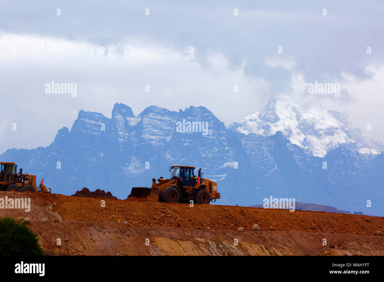 Heavy machinery working moving earth, the start of construction at the site of a new international airport at Chinchero for Cusco and Machu Picchu. In the background is Mt Sawasiray, one of the peaks of the Cordillera Urubamba mountain range. Cusco Region, Peru Stock Photo