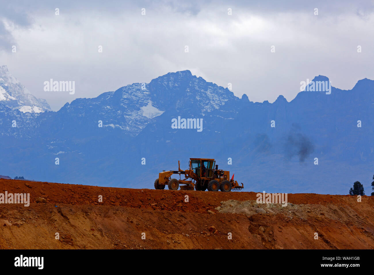 Road grader working moving earth, the start of construction at the site of a new international airport at Chinchero for Cusco and Machu Picchu. In the background are the peaks of the Cordillera Urubamba mountain range. Cusco Region, Peru Stock Photo