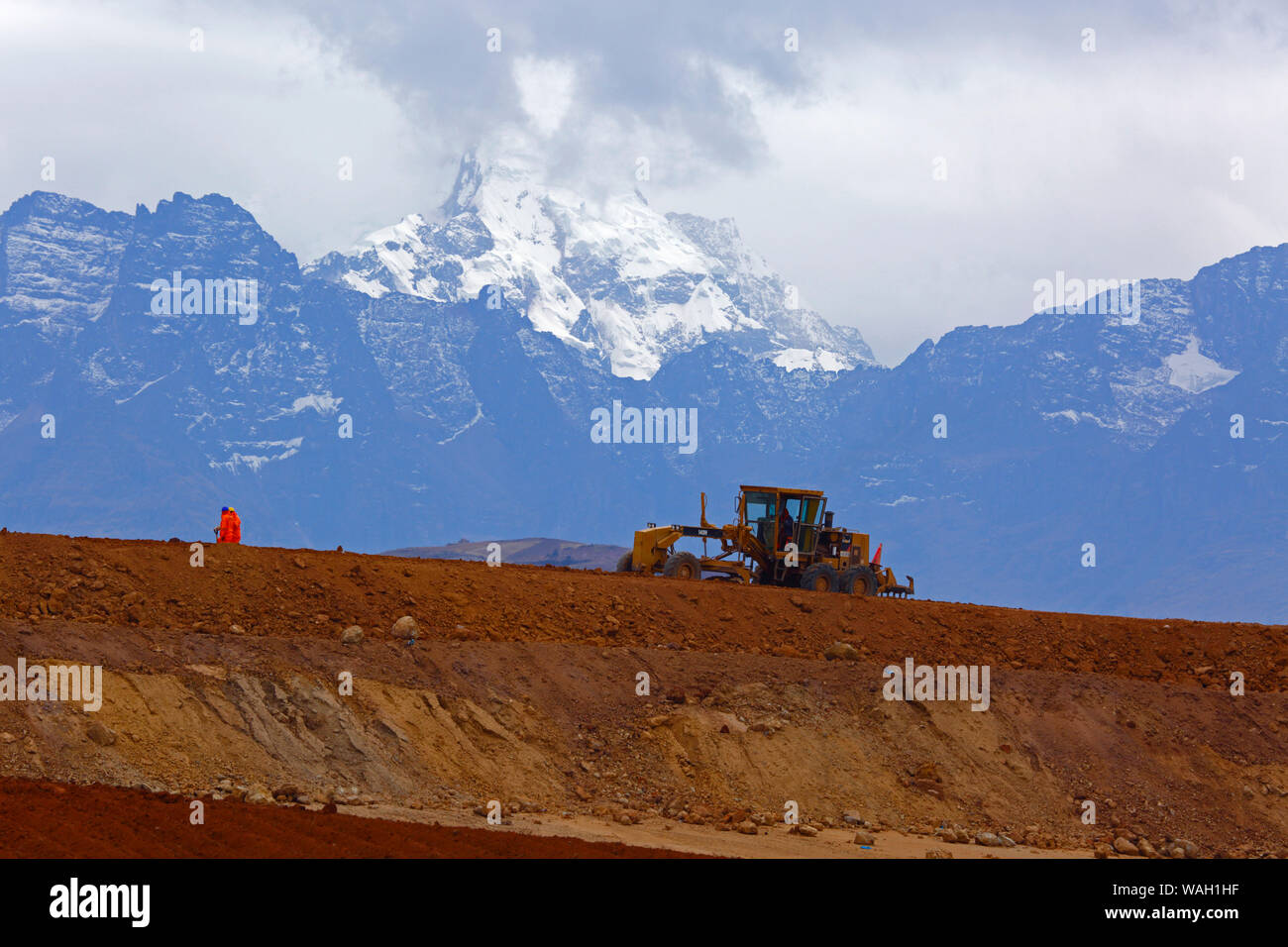 Road grader working moving earth, the start of construction at the site of a new international airport at Chinchero for Cusco and Machu Picchu. In the background is Mt Sawasiray, one of the peaks of the Cordillera Urubamba mountain range. Cusco Region, Peru Stock Photo