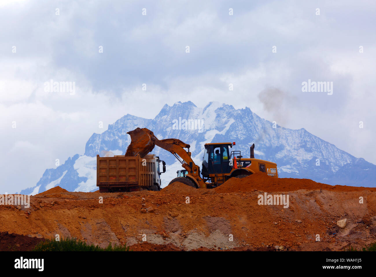 Heavy machinery working moving earth, the start of construction at the site of a new international airport at Chinchero for Cusco and Machu Picchu. In the background is Mt Chicon, one of the peaks of the Cordillera Urubamba mountain range. Cusco Region, Peru Stock Photo