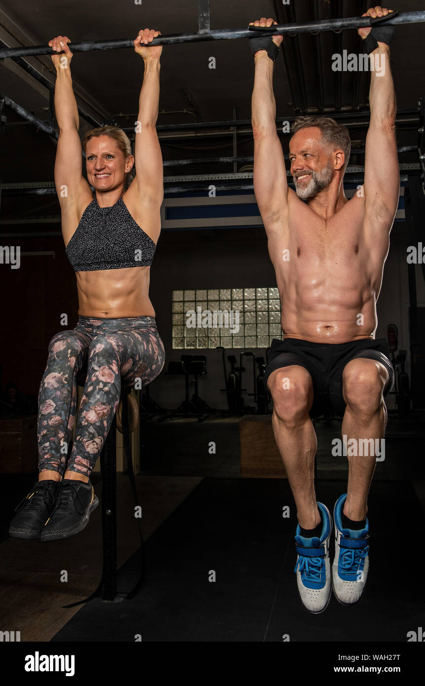A beautiful middle aged couple is doing a fitness training together and having fun. Muscular older man and woman are doing knee raises. Stock Photo