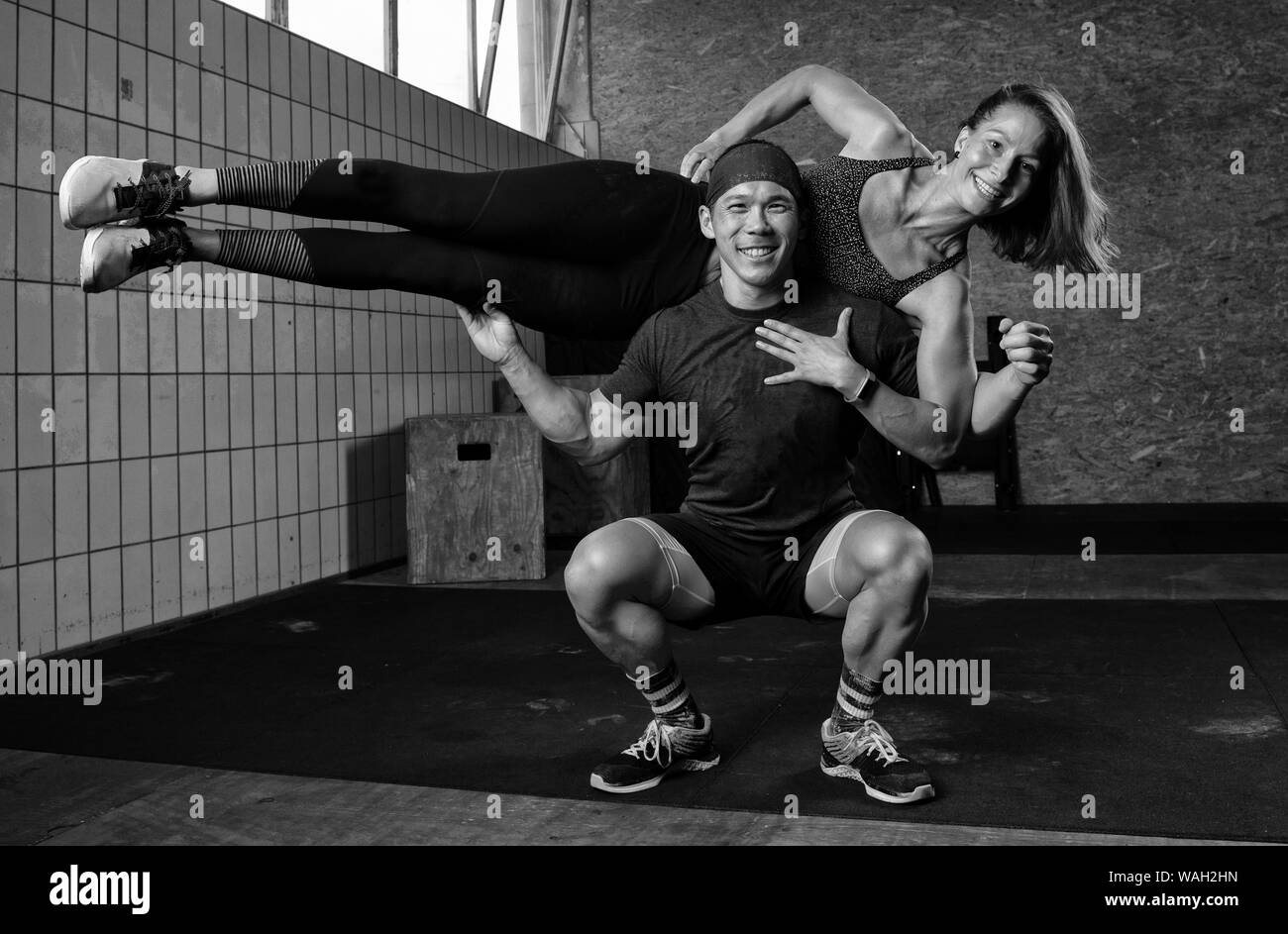 An athletic beautiful couple is smiling, doing a fitness workout together and having fun.The muscular man is holding the fit woman on his shoulders. Stock Photo
