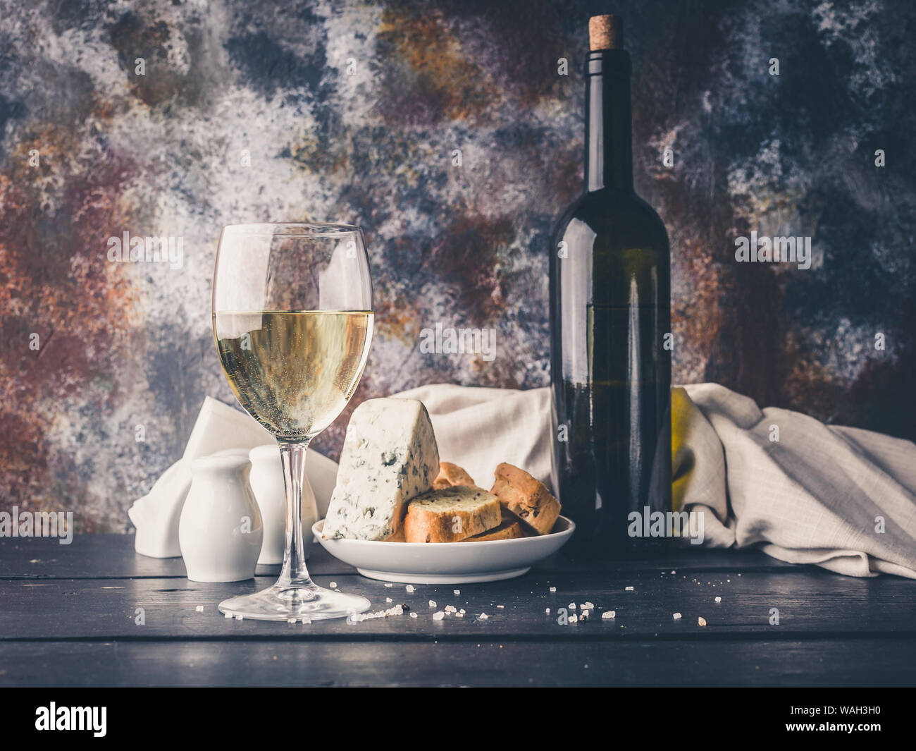 Still life a glass of white wine, cheese, bread and a bottle of wine. Low key lighting Stock Photo