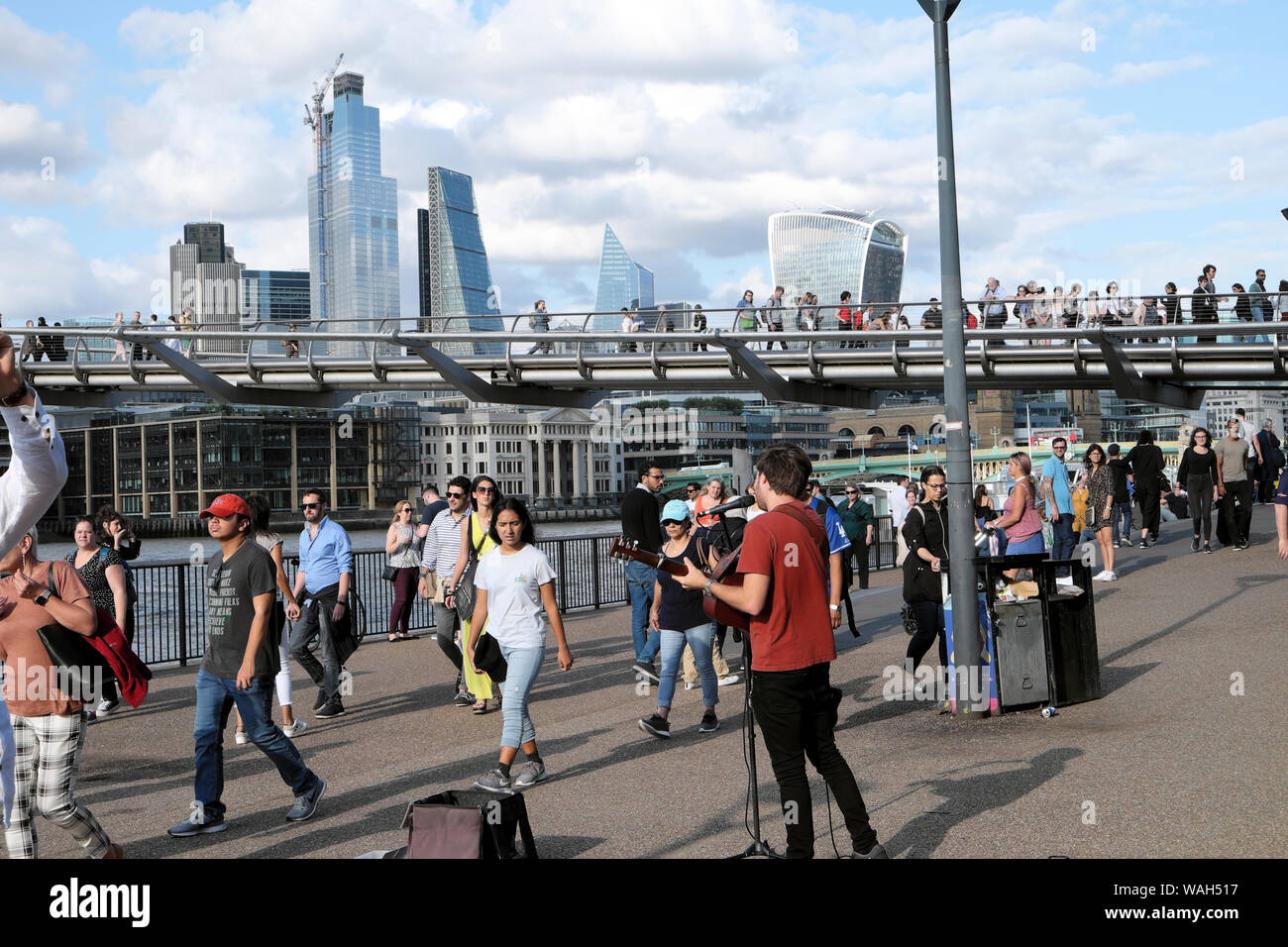 Tourists walking along street & busker busking outside the Tate Modern Art Gallery Bankside with view of City of London England UK  KATHY DEWITT Stock Photo
