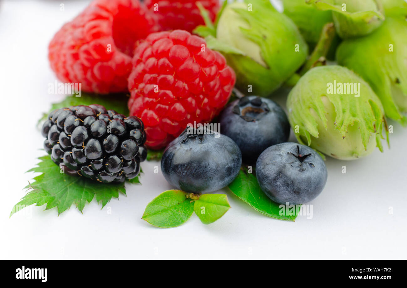 Mix of juicy forest berries and nuts: Raspberries, Blueberries, Blackberry with tiny green leaves and green hazelnuts. Close up, isolated on white. Stock Photo