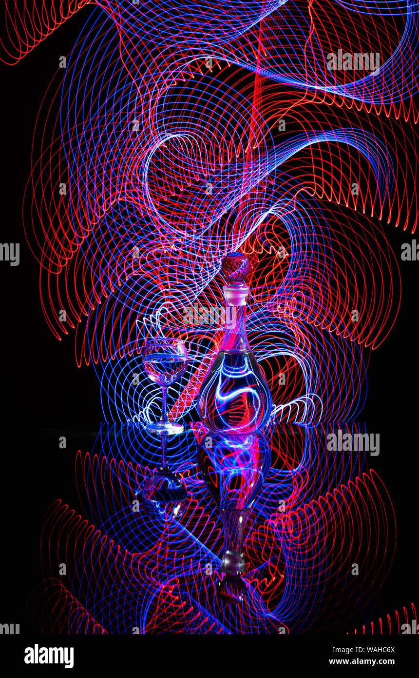 Red and blue light painting behind a wineglass and a jug of wine on a dark background Stock Photo