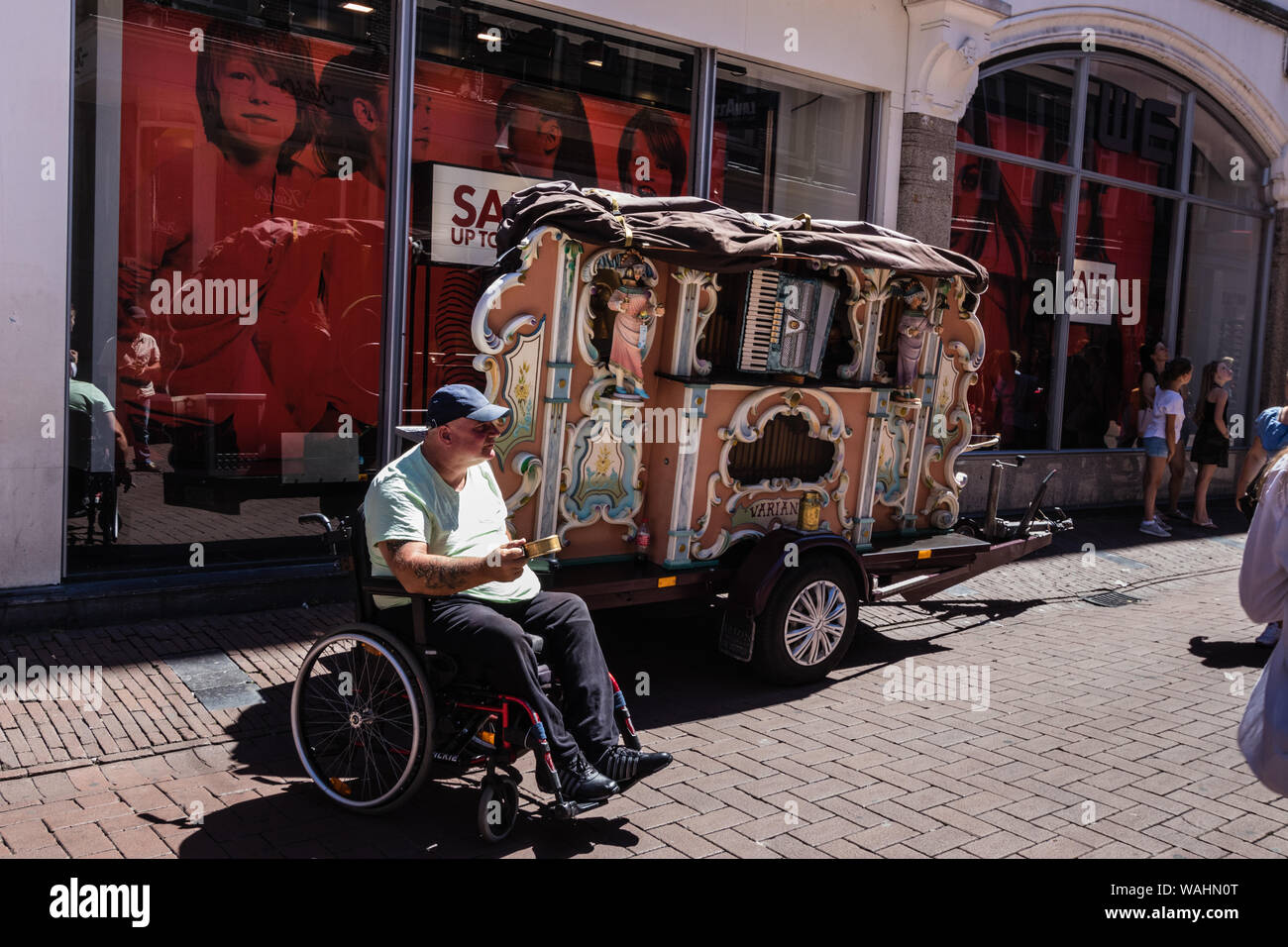 A disabled beggar in a wheelchair with a barrel organ on the street in Amsterdam Stock Photo