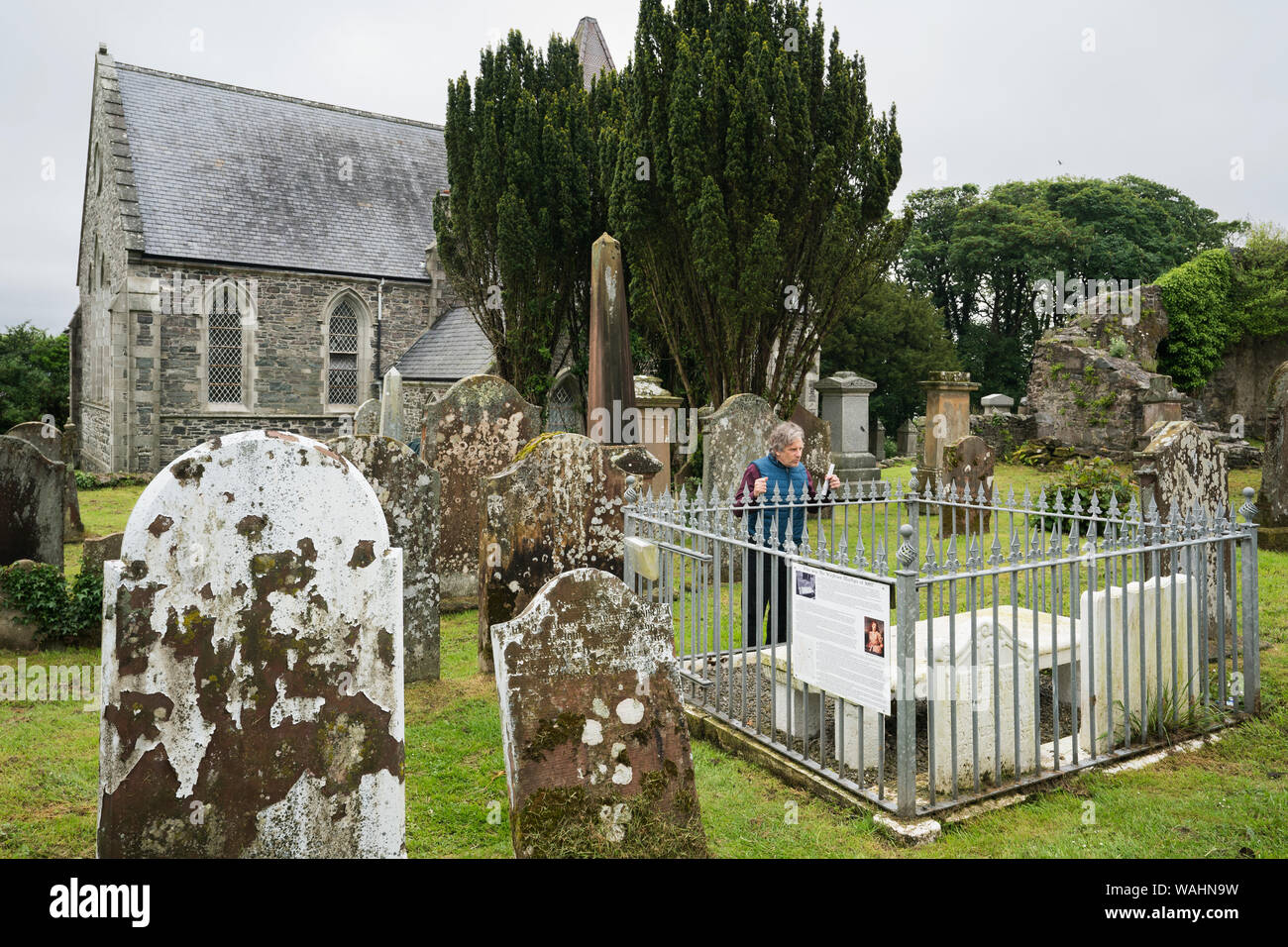 Adult male tourist in a blue vest pays respects to the 2 female Covenanter marytrs buried in the Wigtown Parish Church cemetery on a rainy day, Wigtow Stock Photo