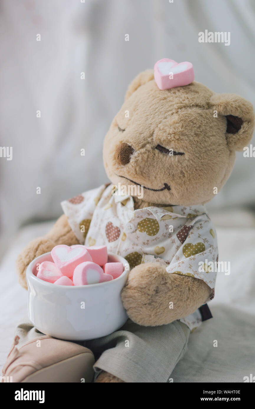 Brown Teddy bear holding pink heart shape marshmallow Stock Photo