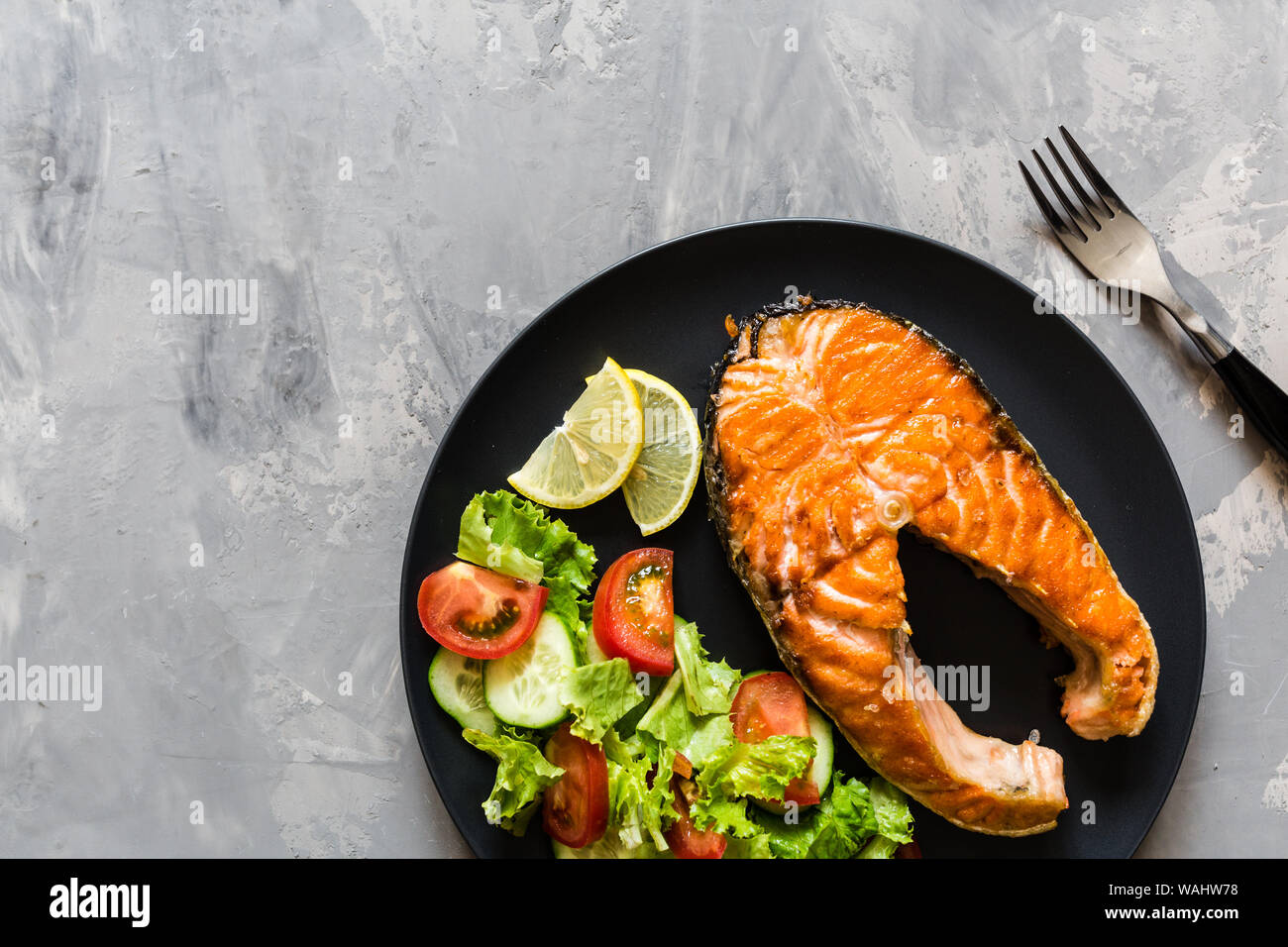 Fried salmon fish steak with vegetable salad and lemon on black plate ...