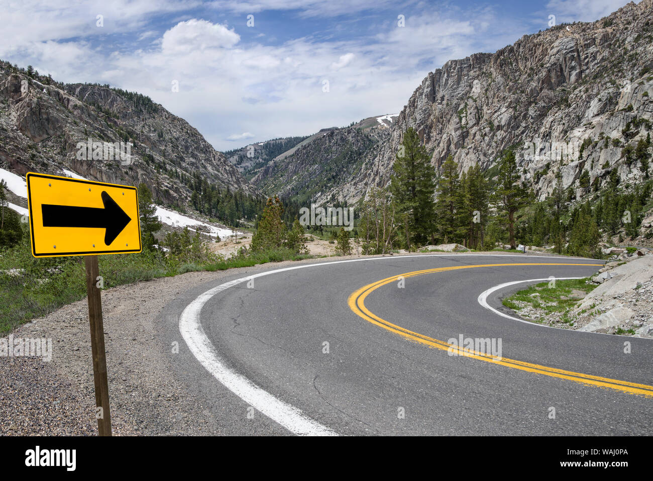 Sharp Turn Warning Arrow:  A sign points the way along a winding road through the Sierra Nevada Mountains. Stock Photo