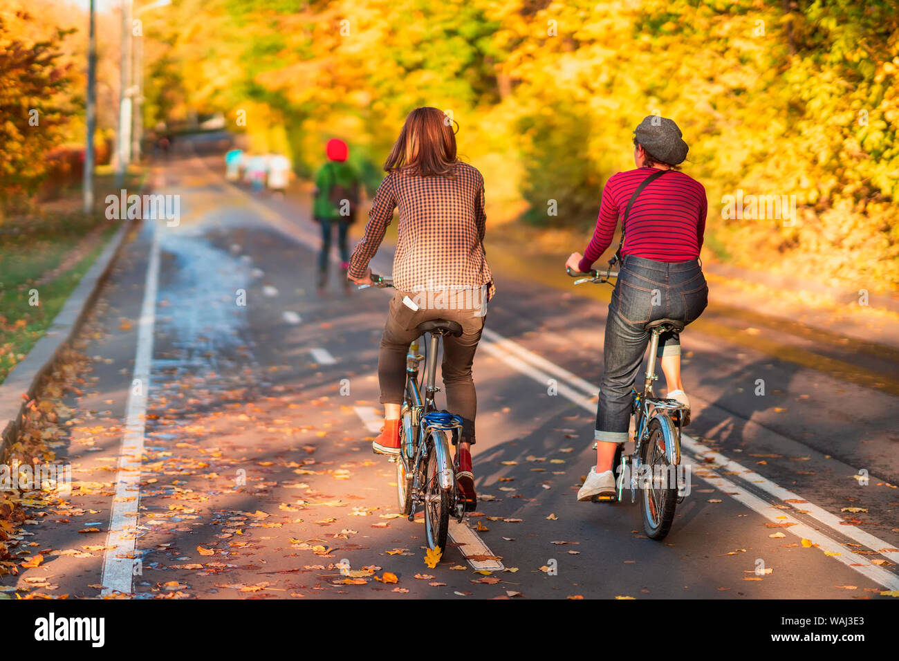 Unrecognizable girls riding bike in autumn park, bright colorful trees, sunny day, fall foliage background. Healthy lifestyle, leisure activity Stock Photo