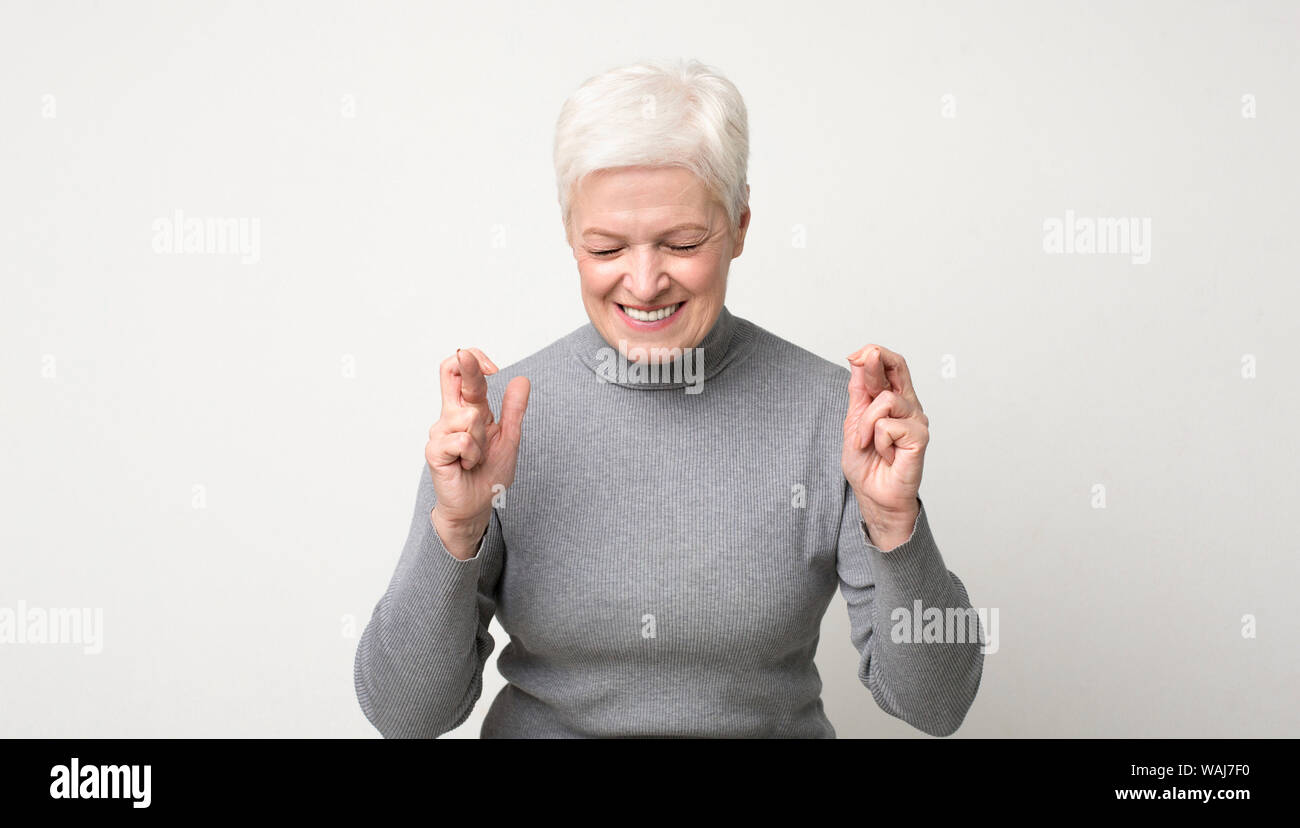Optimistic senior woman crossing fingers with hope with closed eyes Stock Photo