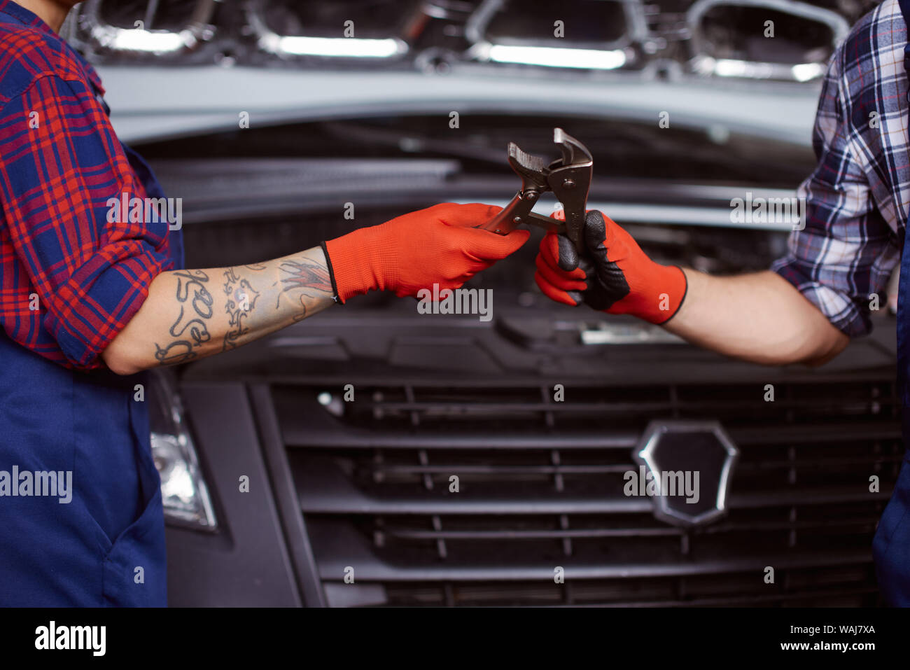 Close up of a man in orange gloves passing instrument to his colleague at the car repair centre. Stock Photo