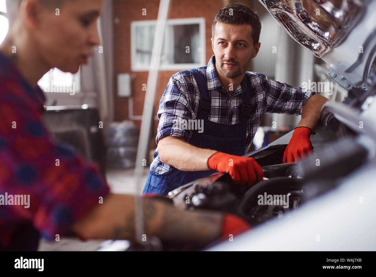 Automechanic teaches his colleague how to clean the engine of such a big car and looks at what she does. Stock Photo