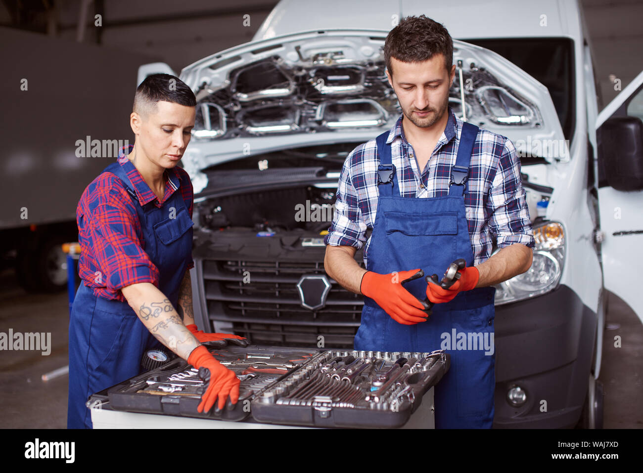 Two people working at the car repair workshop together as they fix the mechanical part of it with the help of numerous instruments. Stock Photo