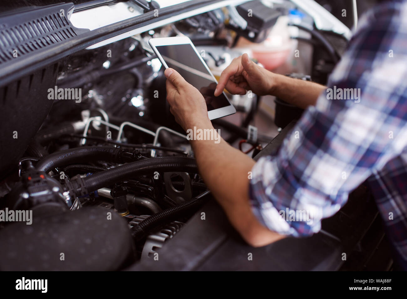 Close up of a man fixing broken car engine while also looking for the spare parts on the market. Stock Photo