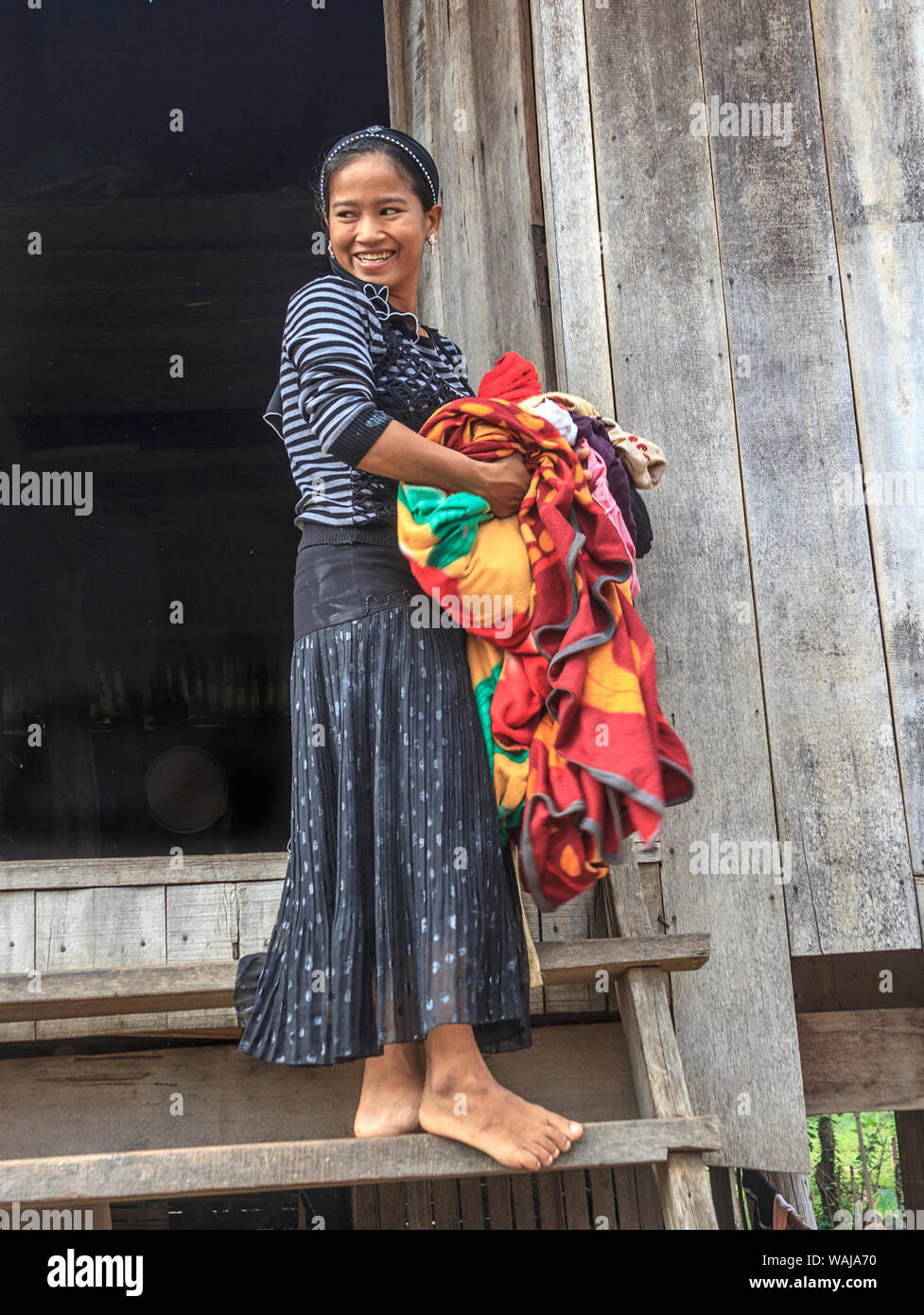 Kratie, Cambodia. Young Cham girl carries laundry up the steps of her house in a village along the Mekong River. The Cham are the largest ethnic minority in Cambodia and are mostly Muslim. Stock Photo