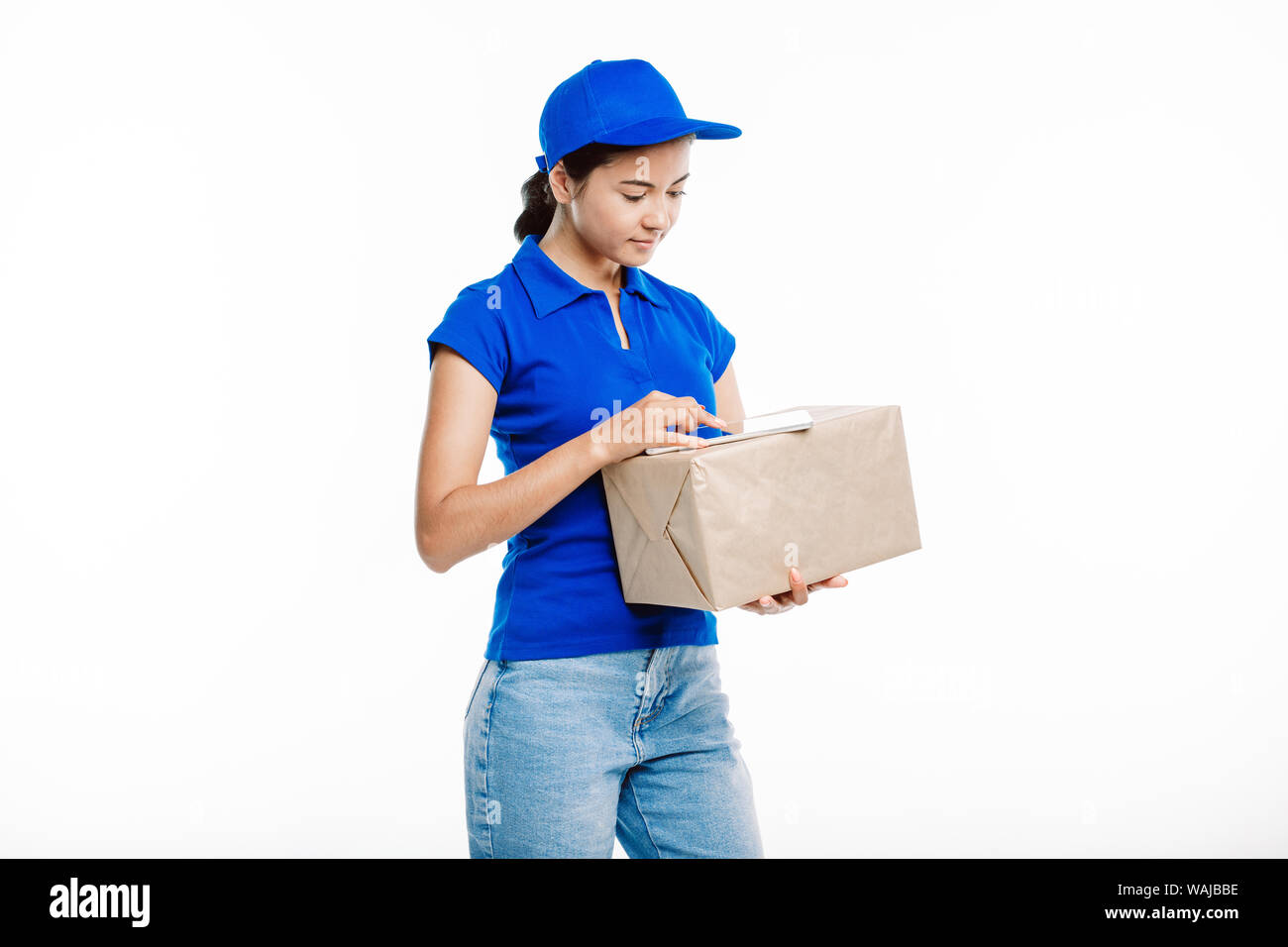 Girl in the post office uniform goes through the feed on her tablet as she holds the big parcel. Stock Photo