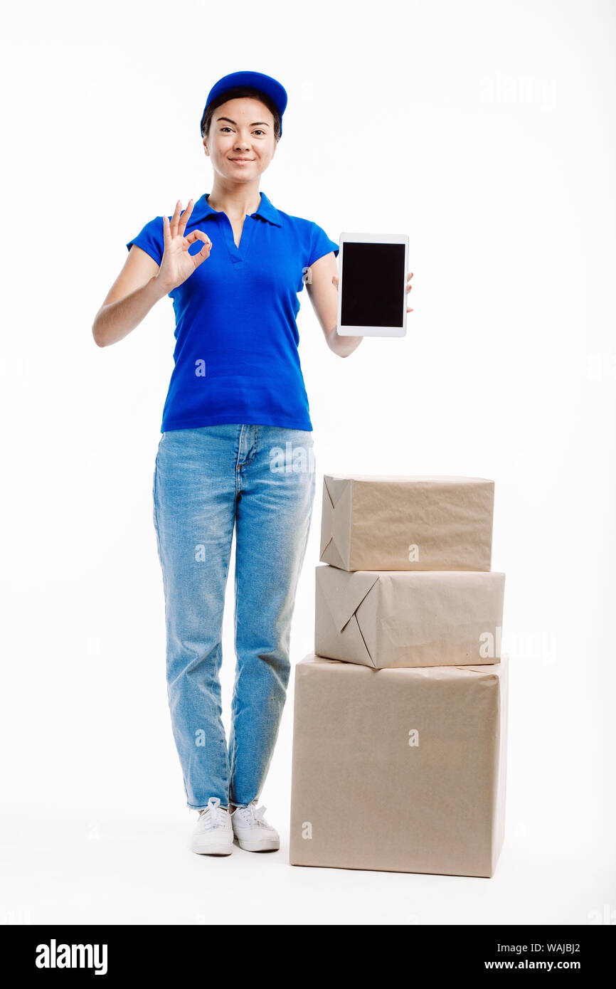 Woman working in delivery has three parcels by her side as she holds a tablet in front of her. Stock Photo