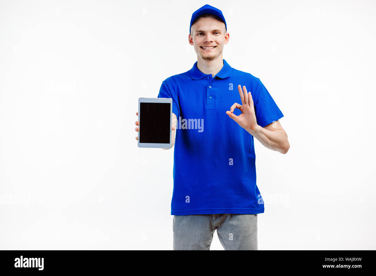 Delivery guy turns tablet screen towards the camera, smiles and does OK sign with his other hand. Stock Photo