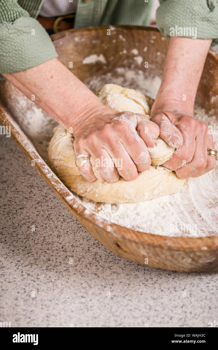 Woman kneading dough in an antique dough trough until it is smooth and elastic, as part of making sprouted wheat bread. (MR) Stock Photo