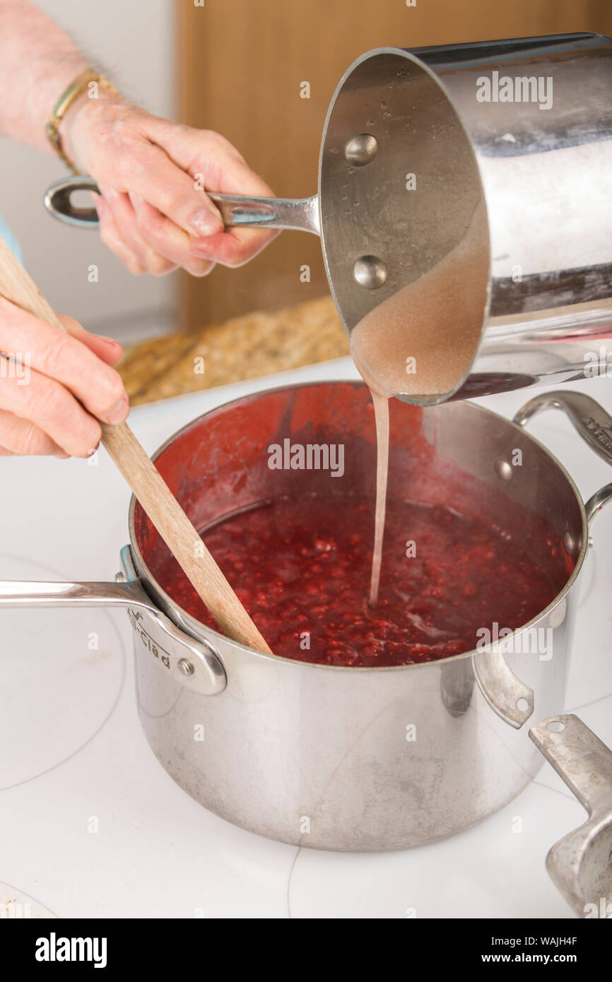 Woman pouring fruit pectin and water mixture into raspberries as a part of making raspberry jam. (MR,PR) Stock Photo