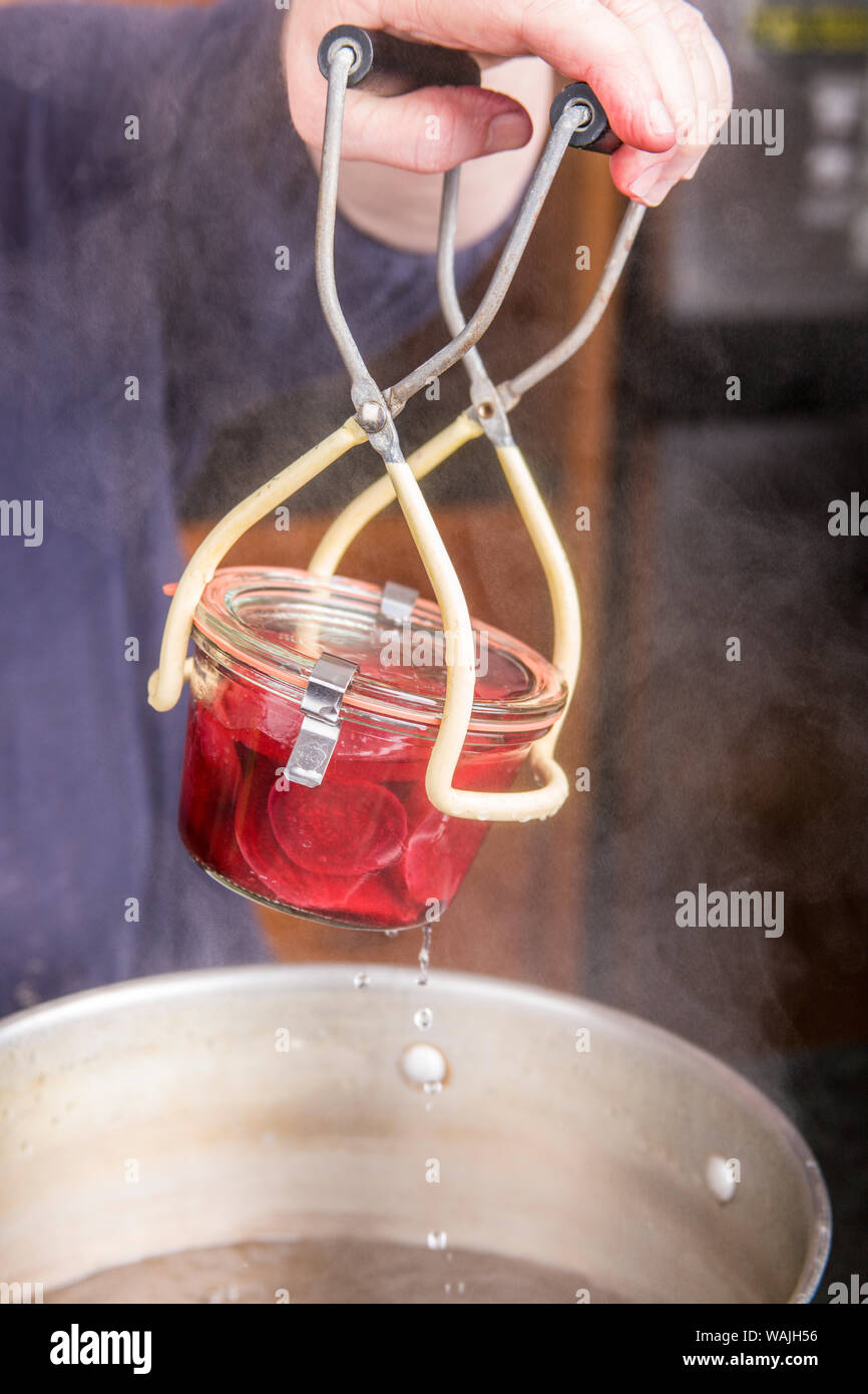 Woman removing a Weck canning jar of pickled beets from a boiling water