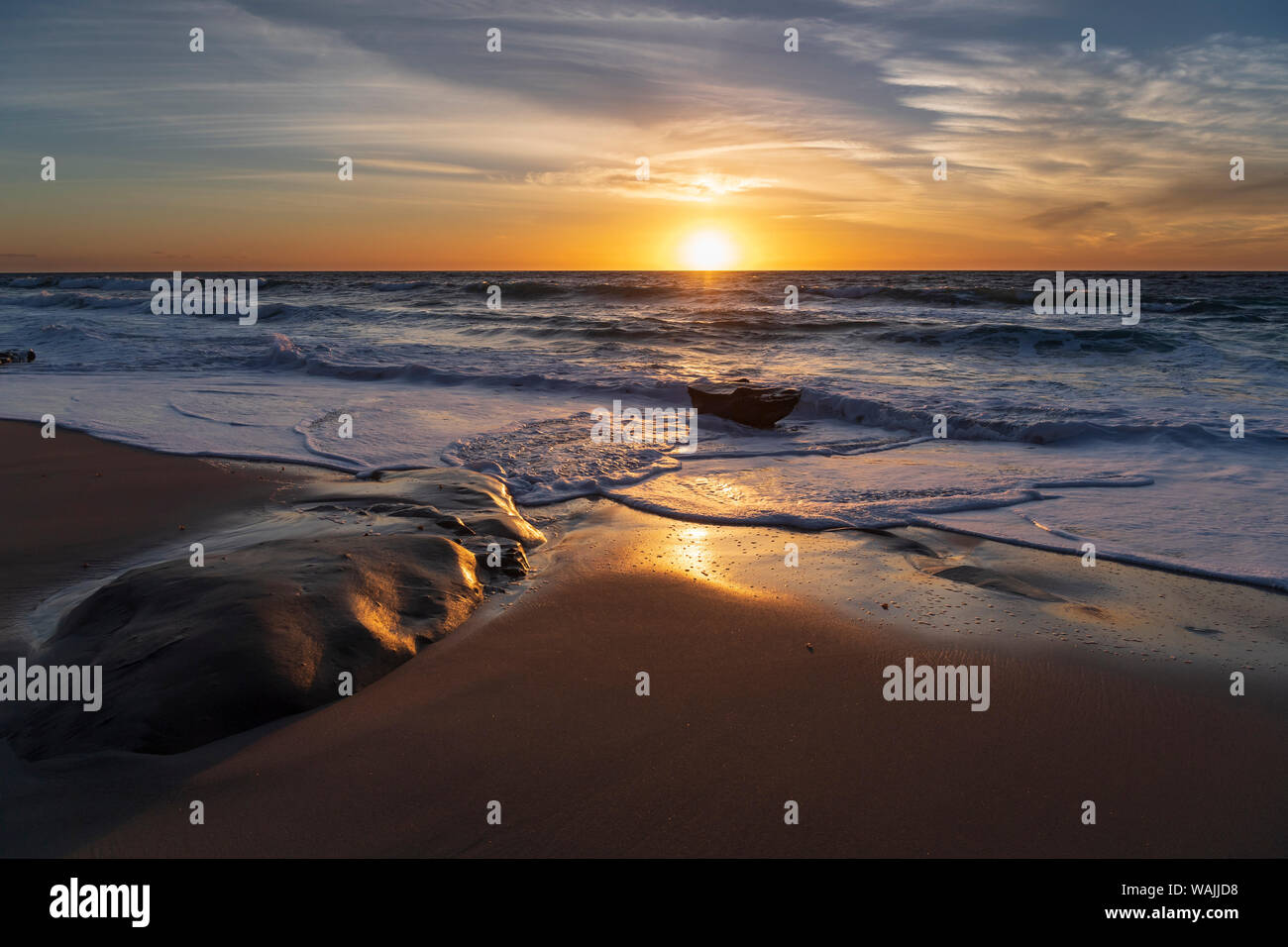 Sunset reflecting off the water on the sand of a beach Stock Photo