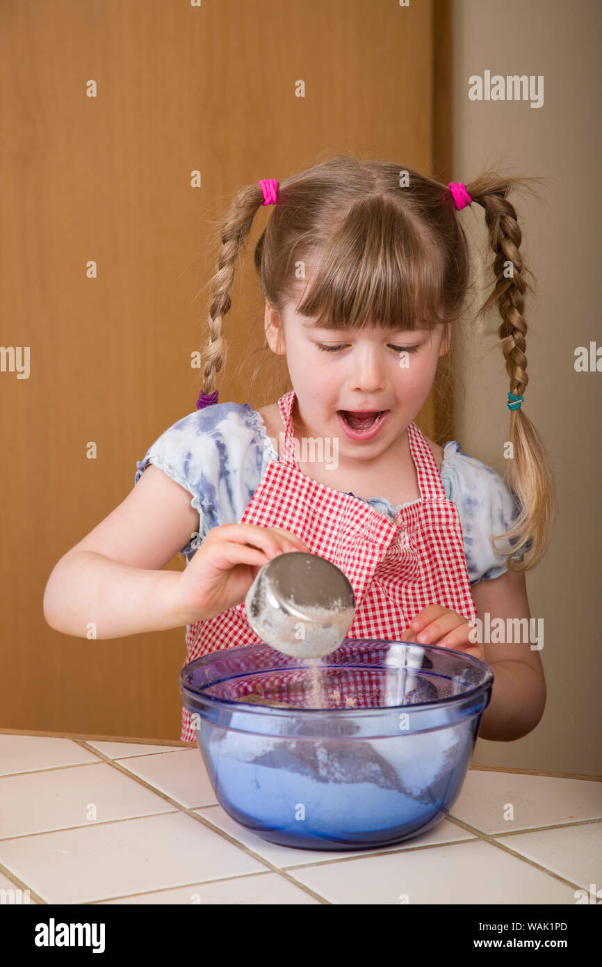 Girl pouring sugar into mixing bowl, with an astonished look on her face, as she helps make carrot cake. (MR, PR) Stock Photo