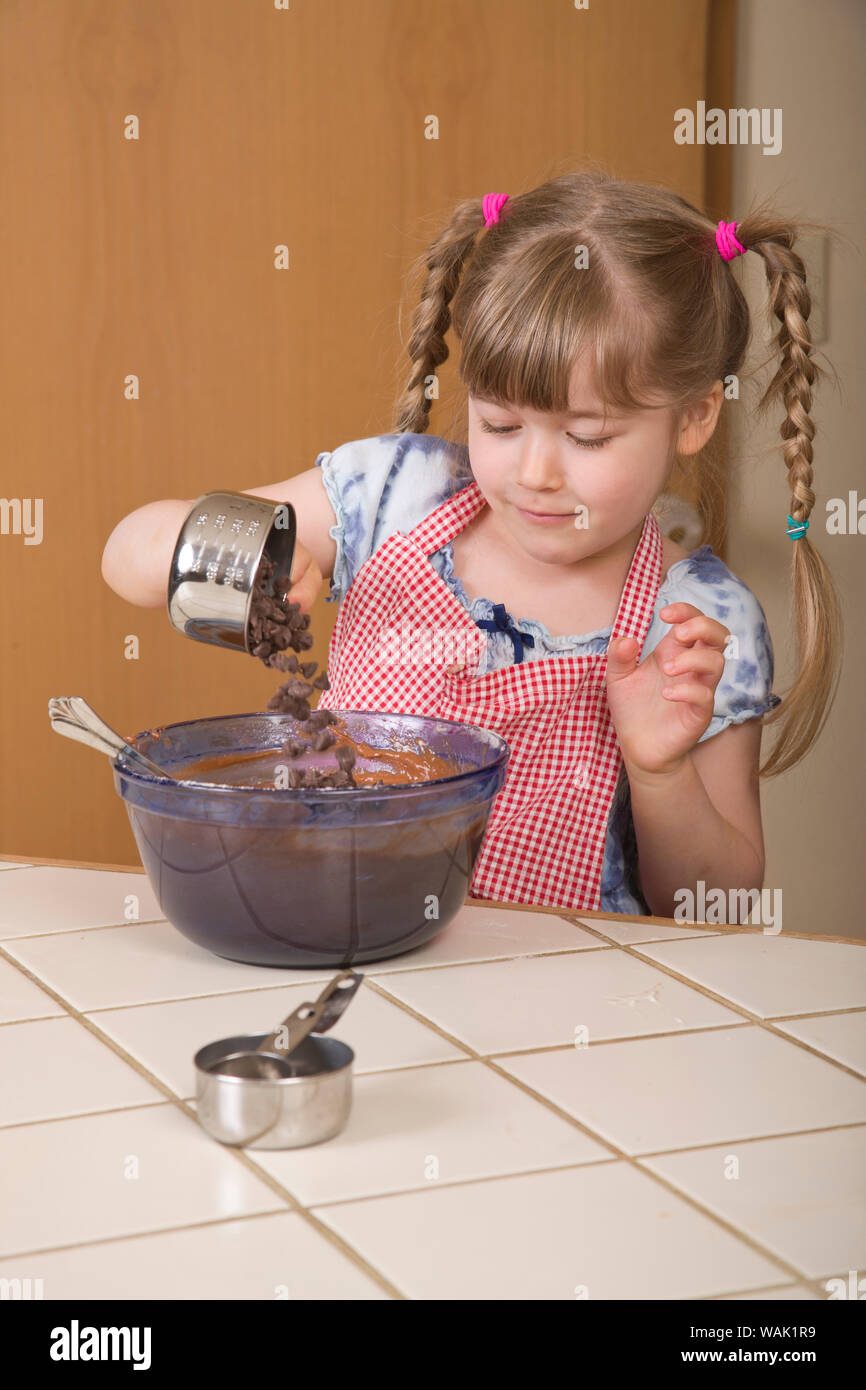 Girl pouring chocolate chips into a chocolate bundt cake in mixing bowl. (MR, PR) Stock Photo