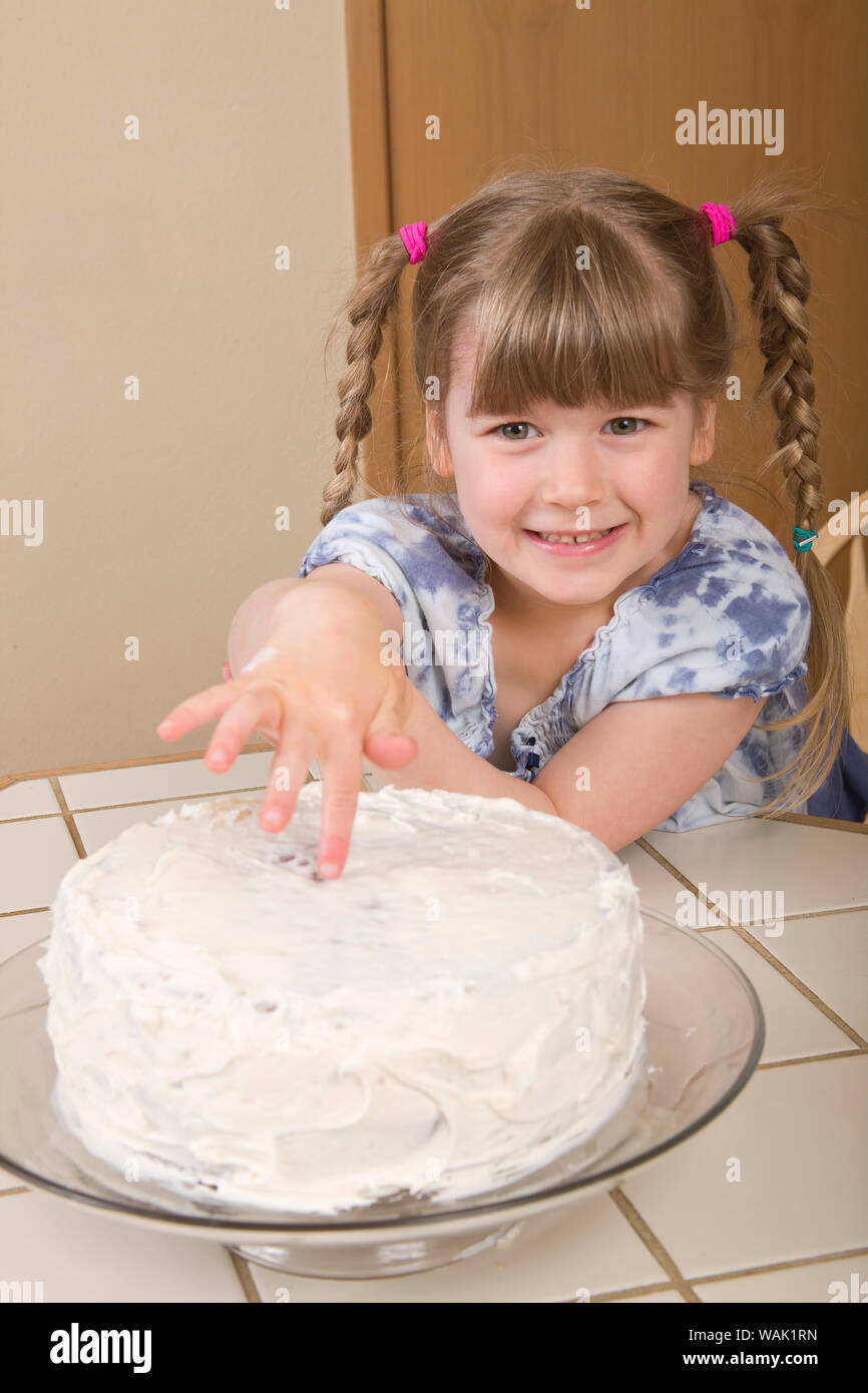 Girl placing her finger in the middle of cream frosting of a carrot cake, trying to sneak a bite of frosting. (MR, PR) Stock Photo
