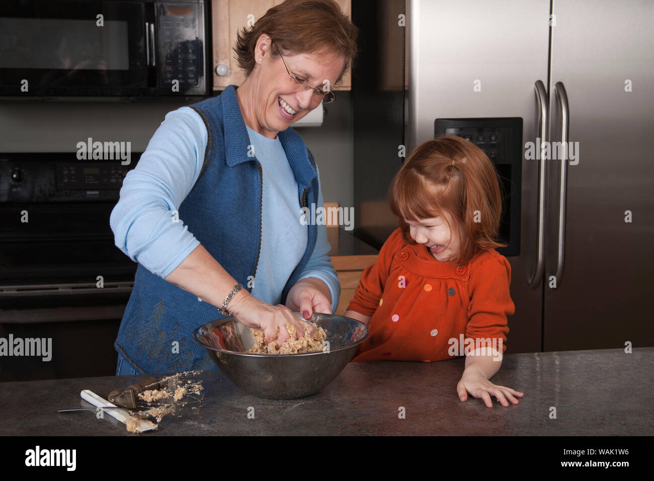 Grandmother mixing cookie dough with 4 year old granddaughter looking on. (MR, PR) Stock Photo