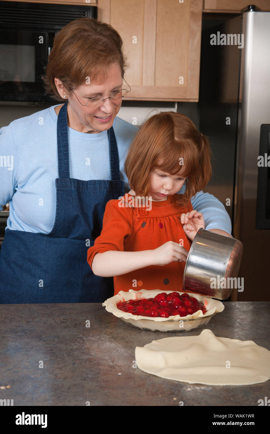 Girl adding cherry pie filling into pie shell with her grandmother assisting. (MR, PR) Stock Photo