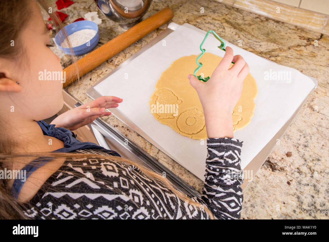 Girl using cookie cutters to cut out Christmas sugar cookies. (MR, PR) Stock Photo