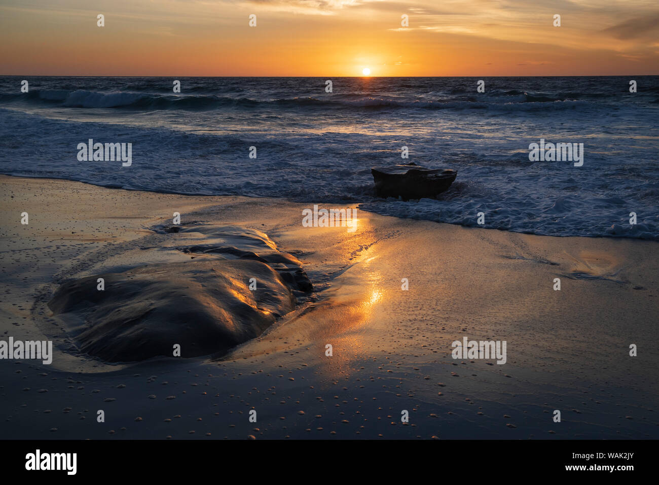 Sunset reflecting off the water on the sand of a beach Stock Photo
