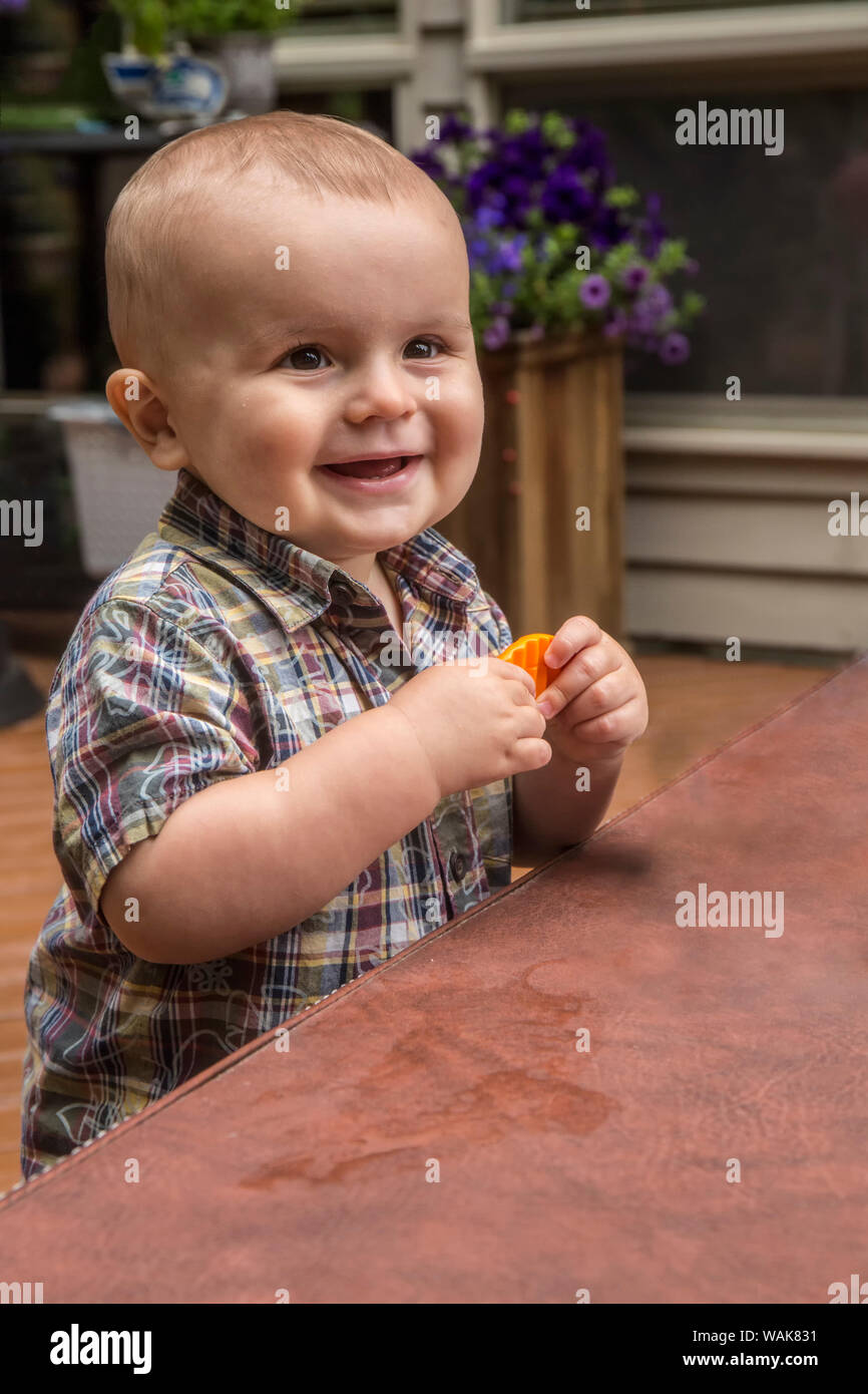 Issaquah, Washington State, USA. Fourteen month old happy toddler boy playing with a plastic carrot outside, using a spa cover for a table. (MR,PR) Stock Photo