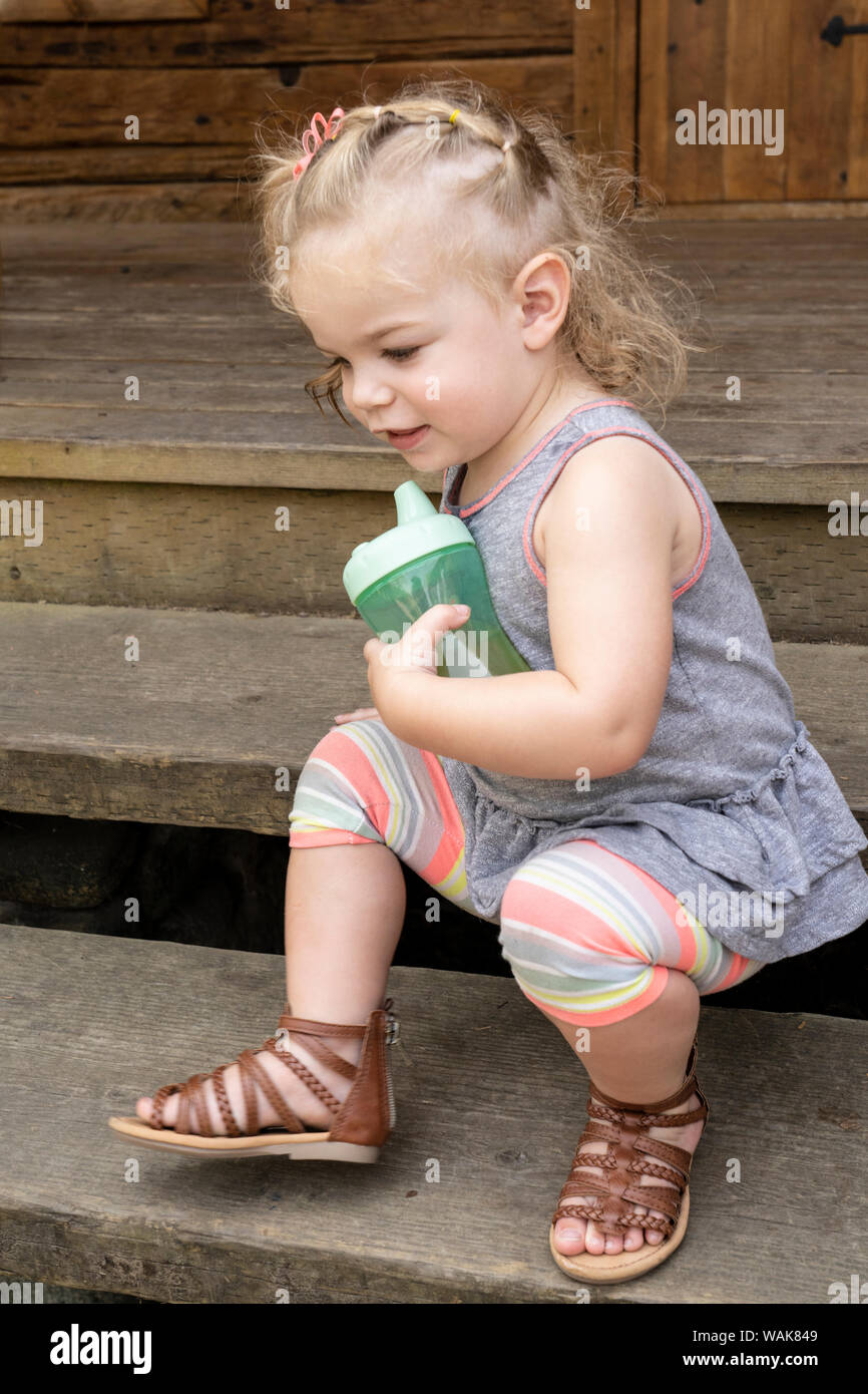 Bellevue, Washington State, USA. Twenty month old girl scooting down some steps while holding her sippy cup. (MR) Stock Photo