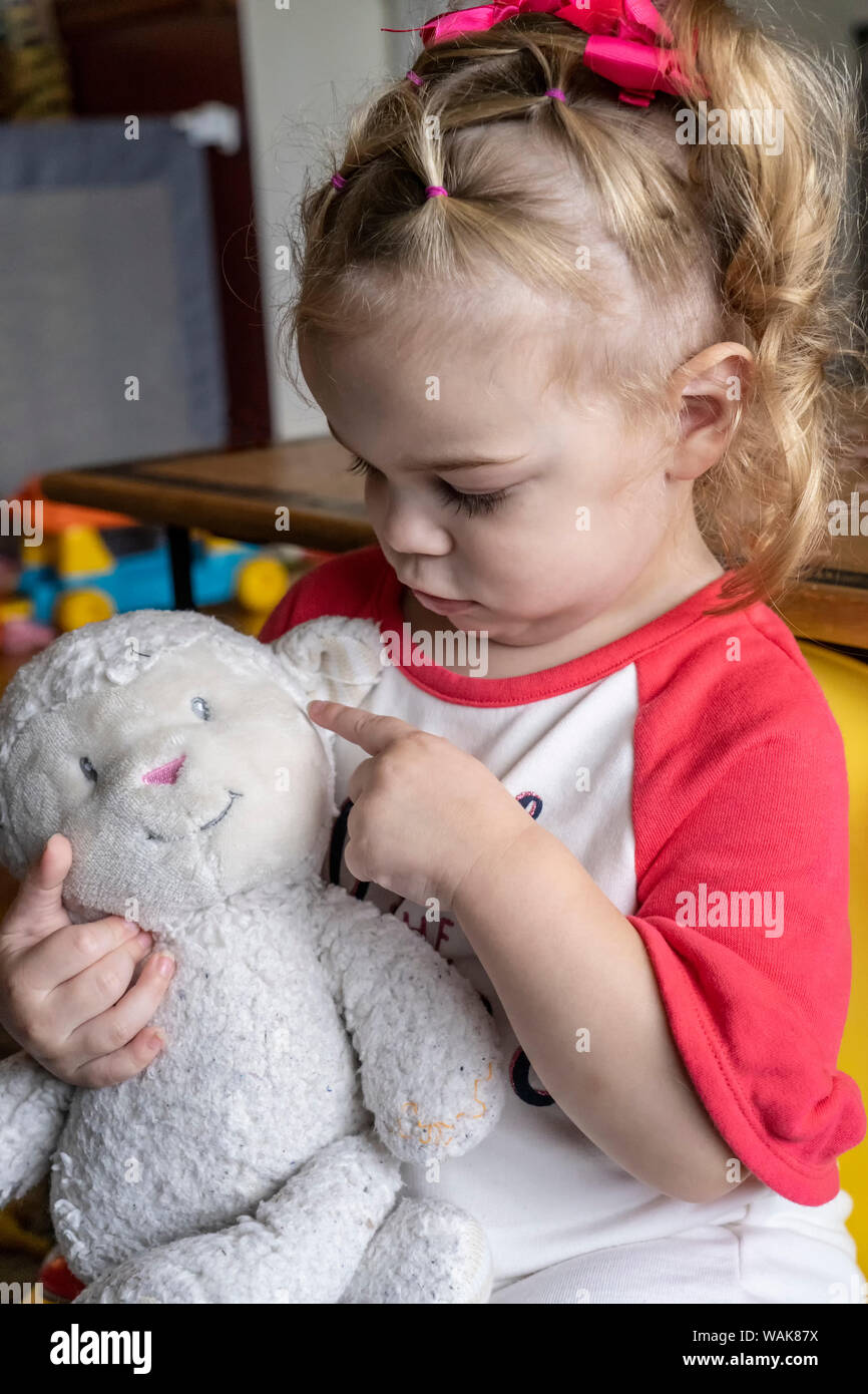 22 month old girl playing with her lamb stuffed animal, pointing to its ear. (MR) Stock Photo