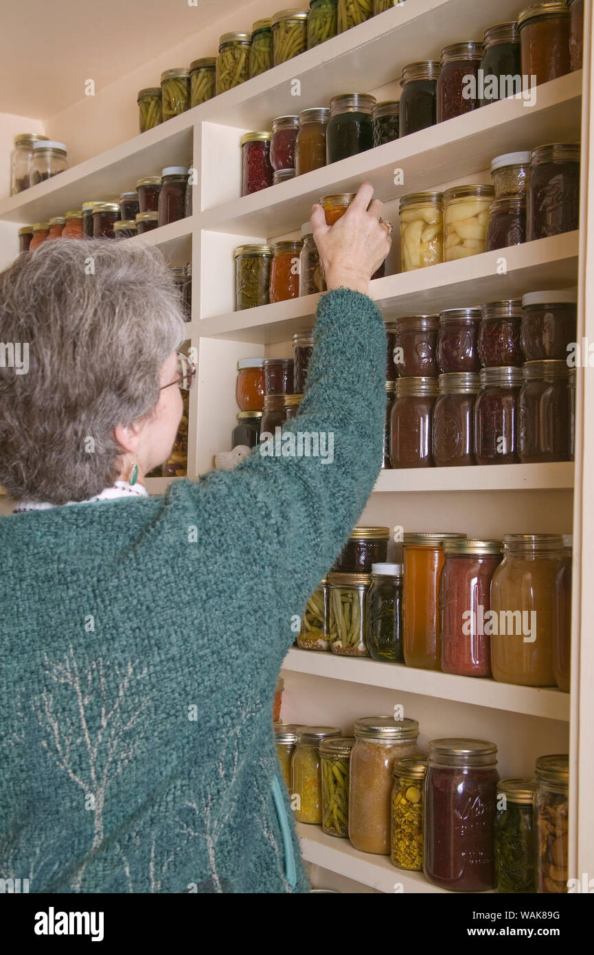 Woman in pantry of preserved fruits and vegetables in canning jars. (MR,PR) Stock Photo