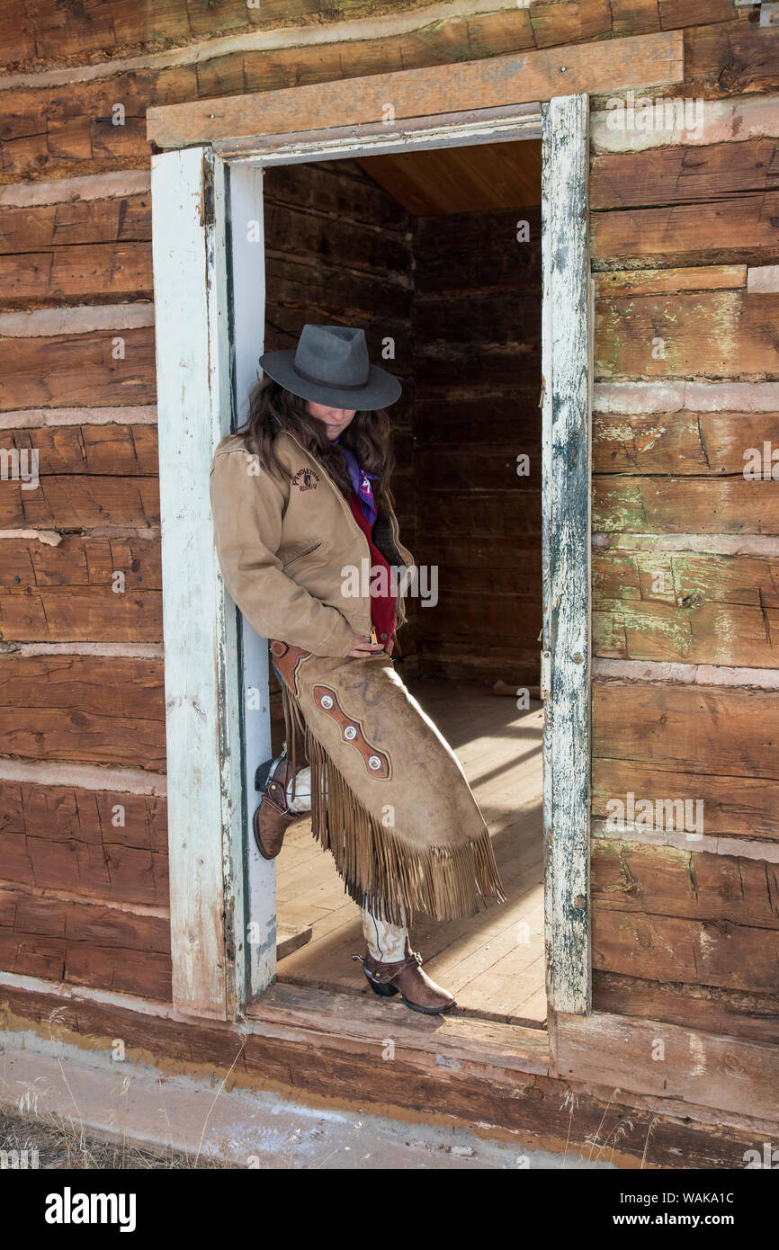 Horse drive in winter on Hideout Ranch, Shell, Wyoming. Cowgirl standing in doorway of old log cabin. (MR) Stock Photo