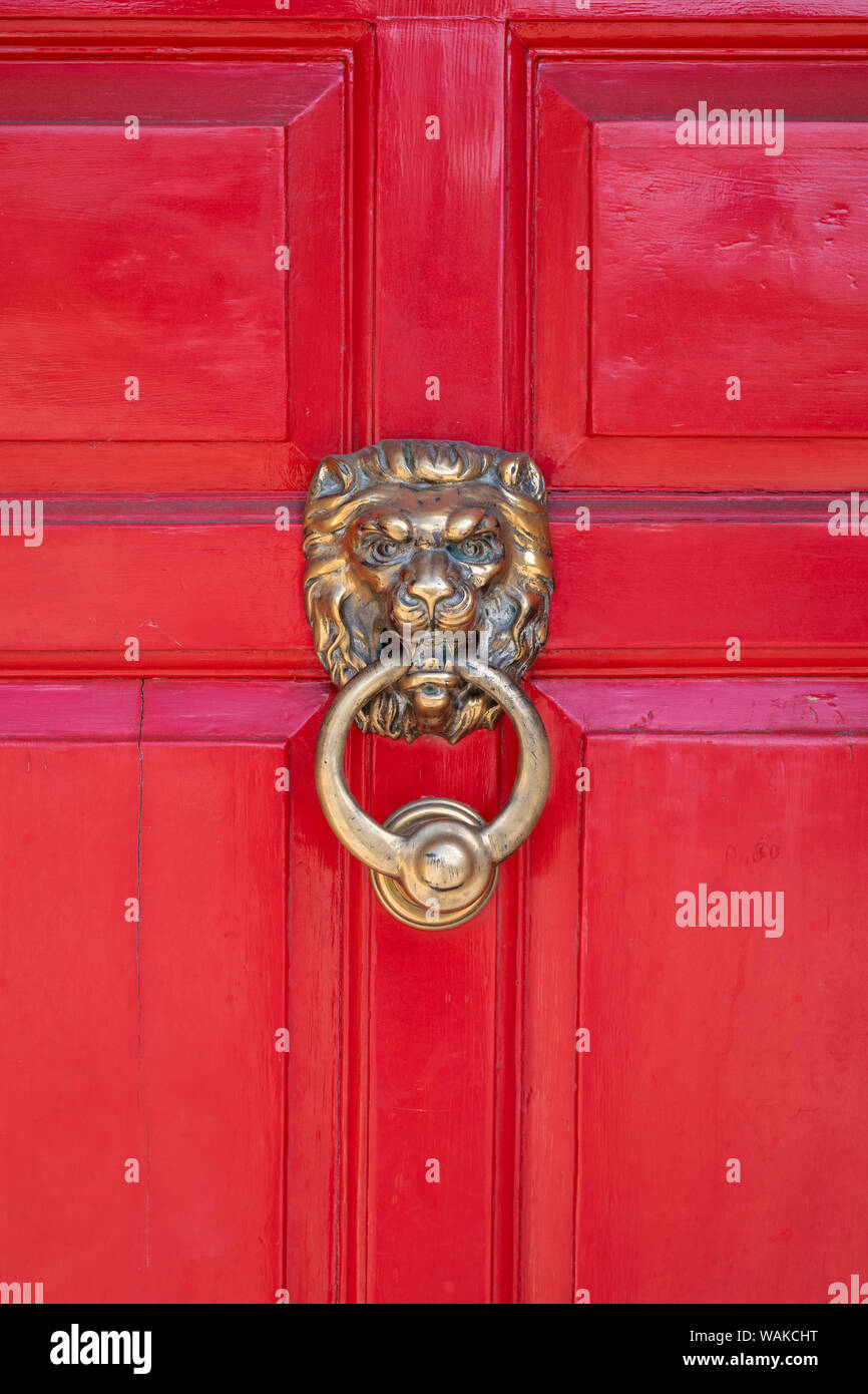 Brass Lions head door knocker on a red wooden door in the ancient Anglo Saxon town of Winchcombe, Cotswolds, Gloucestershire, England Stock Photo