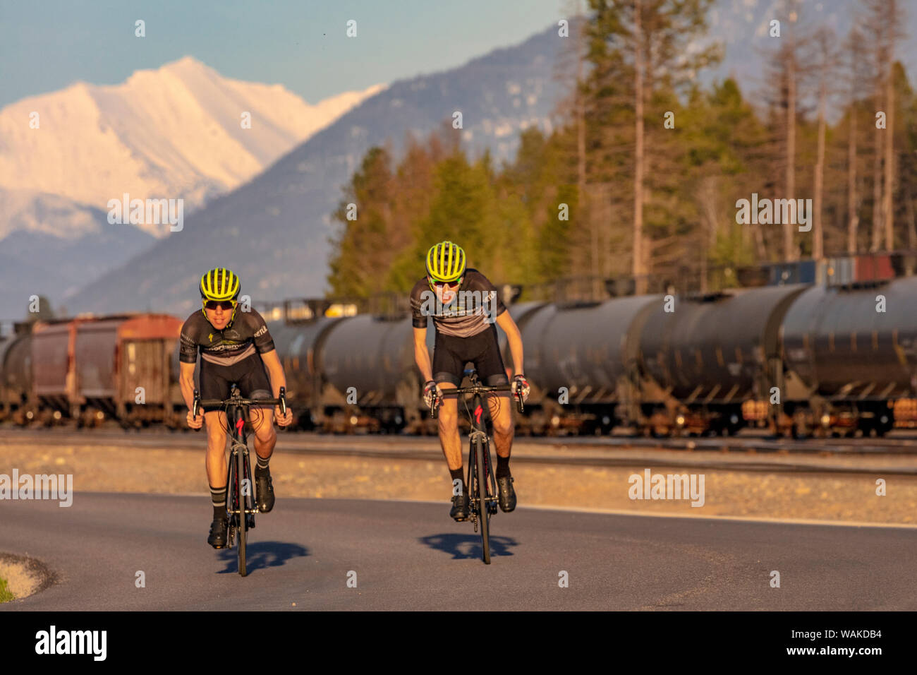 Teenagers road bicycling on Edgewood Road with Great Northern Mountain and railyard in the background in Whitefish, Montana, USA (MR) Stock Photo