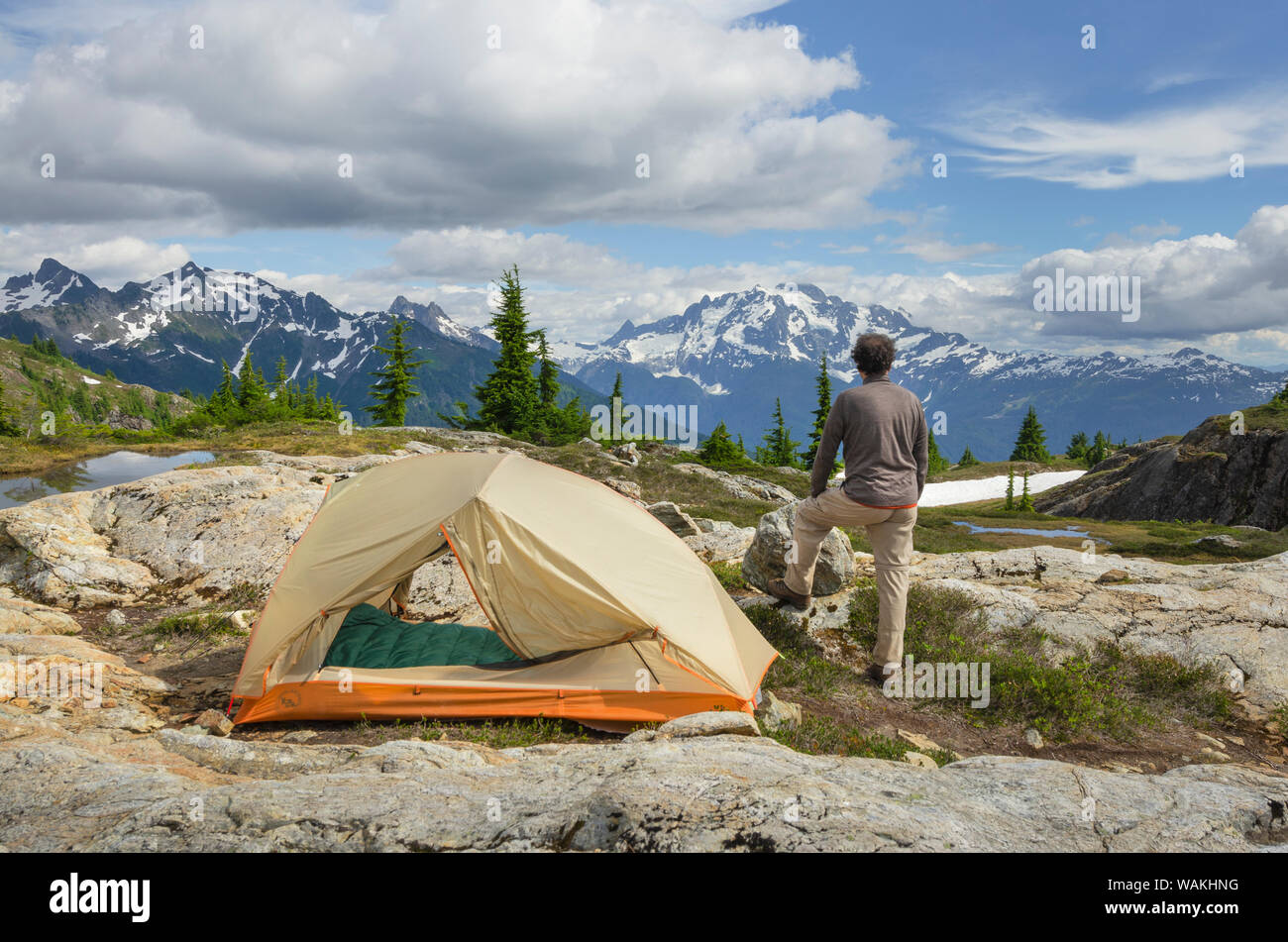 Adult man admiring view from backcountry campsite. Yellow Aster Butte Basin, Mount Baker Wilderness. Mount Shuksan is in the distance. North Cascades, Washington State Stock Photo