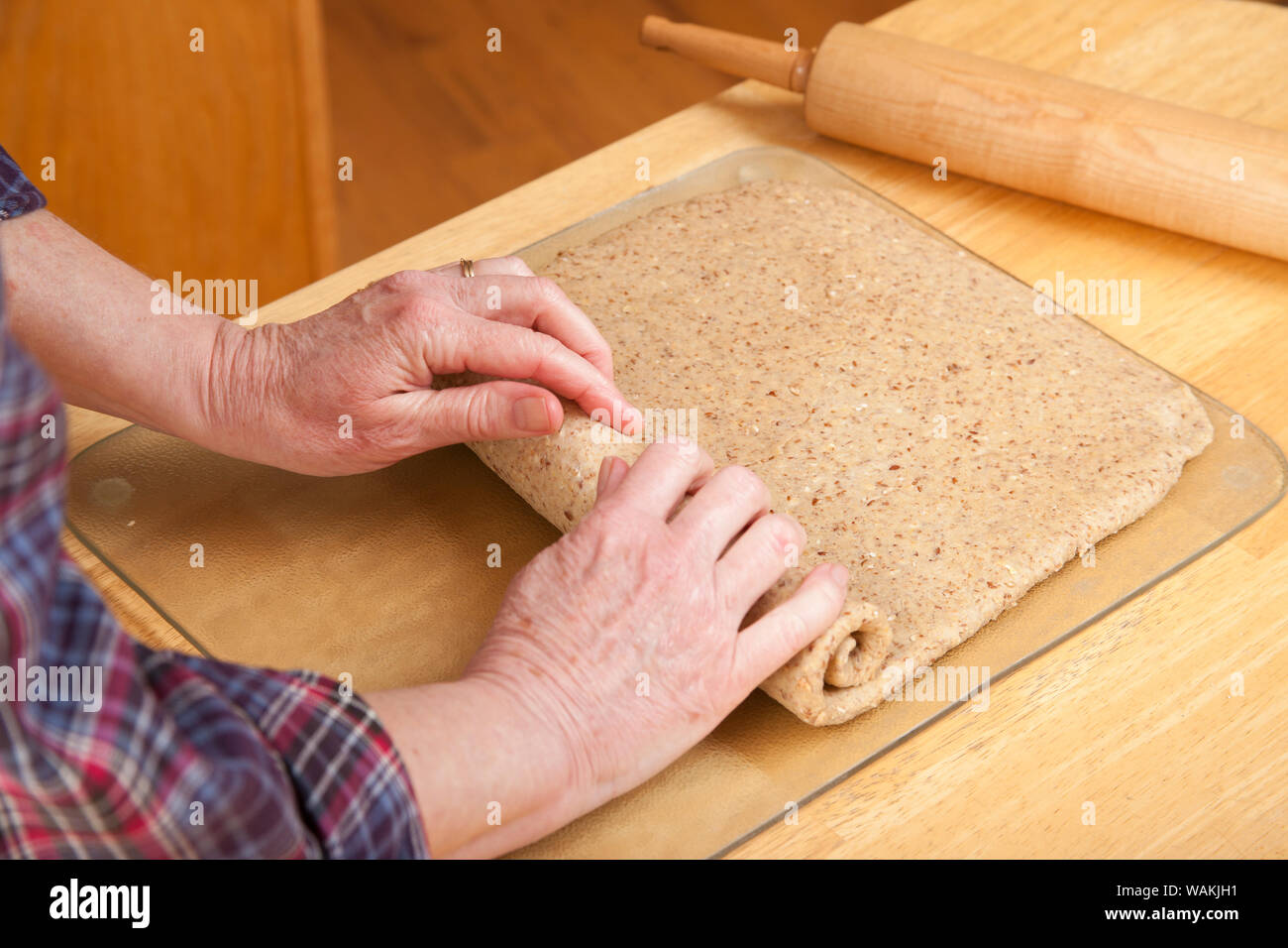 Woman rolling multigrain bead dough into a cylinder shape to make a loaf. (MR) Stock Photo