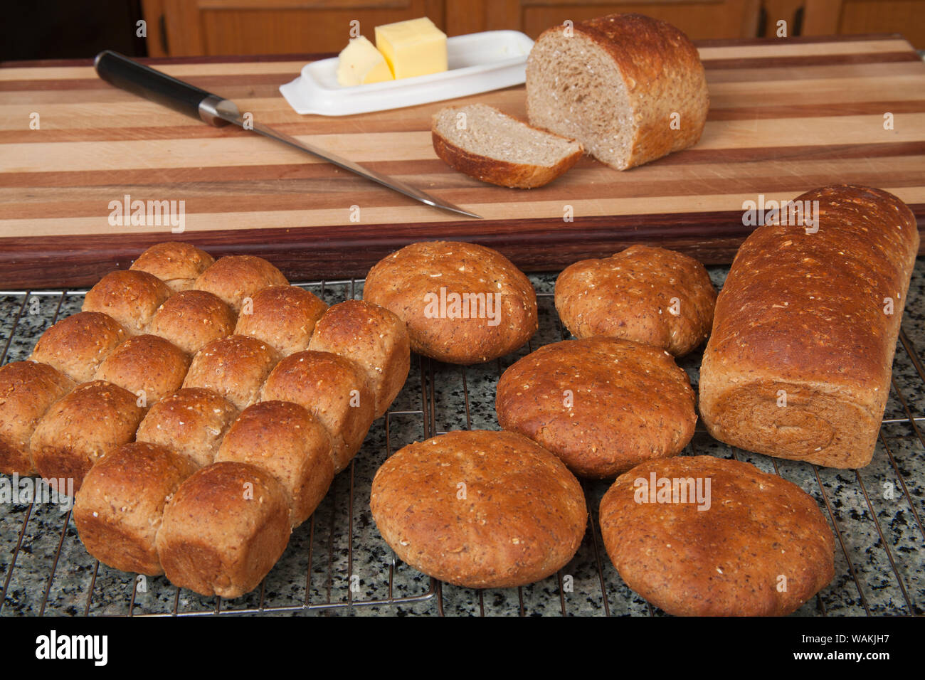 Multigrain rolls, buns and loaf with a slice cut off, with butter and a bread knife. Stock Photo