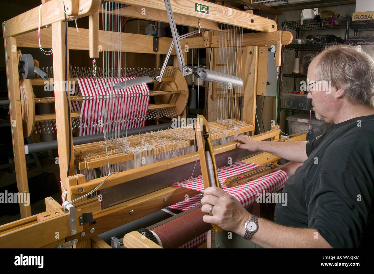 Man using hand shuttle in weaving checkered dish towels on his AVL 16 shaft dobby loom. (MR, PR) Stock Photo