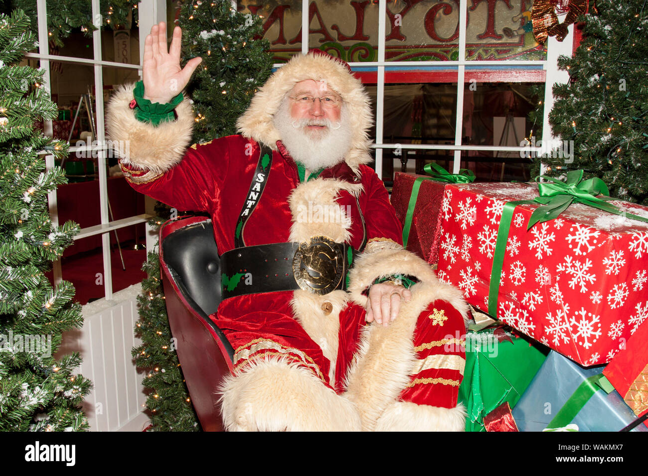 Santa Claus sitting in his sleigh surrounded by wrapped gifts and waving. (MR) Stock Photo