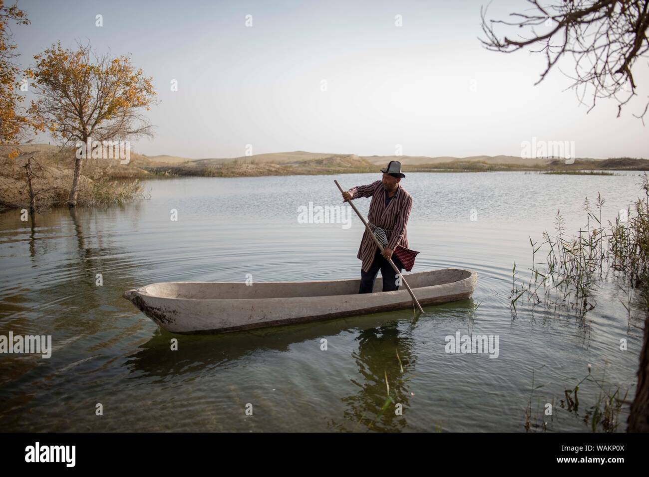 (190821) -- YULI, Aug. 21, 2019 (Xinhua) -- Amudun Abudu rows a canoe for fishing in Lop Nur People Village in Yuli County, northwest China's Xinjiang Uygur Autonomous Region, Oct. 16, 2018. Lop Nur People Village is located in Yuli County, where Tarim River flows through the deserts with populus euphratica forests' reflection on the shimmering waves. Amudun Abudu, a 61-year old typical Lop Nur villager, works in local tourism industry. With the changes of the times, many Lop Nur people have various options for a living, yet he insists on the tradition of fishing in rivers and lakes. Not on Stock Photo
